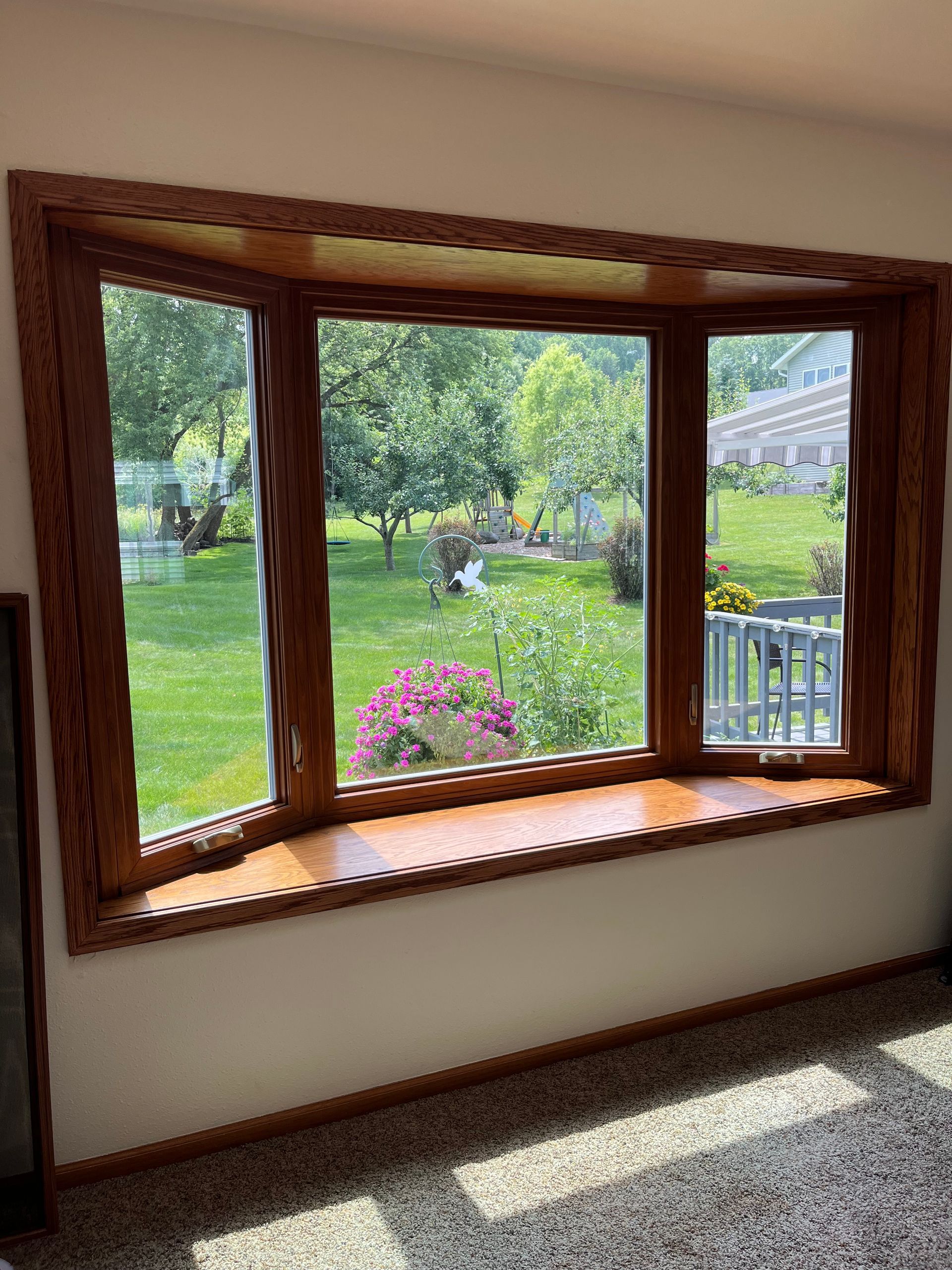 Sunlit bay window overlooking a green garden with a pink flower pot and wooden trim