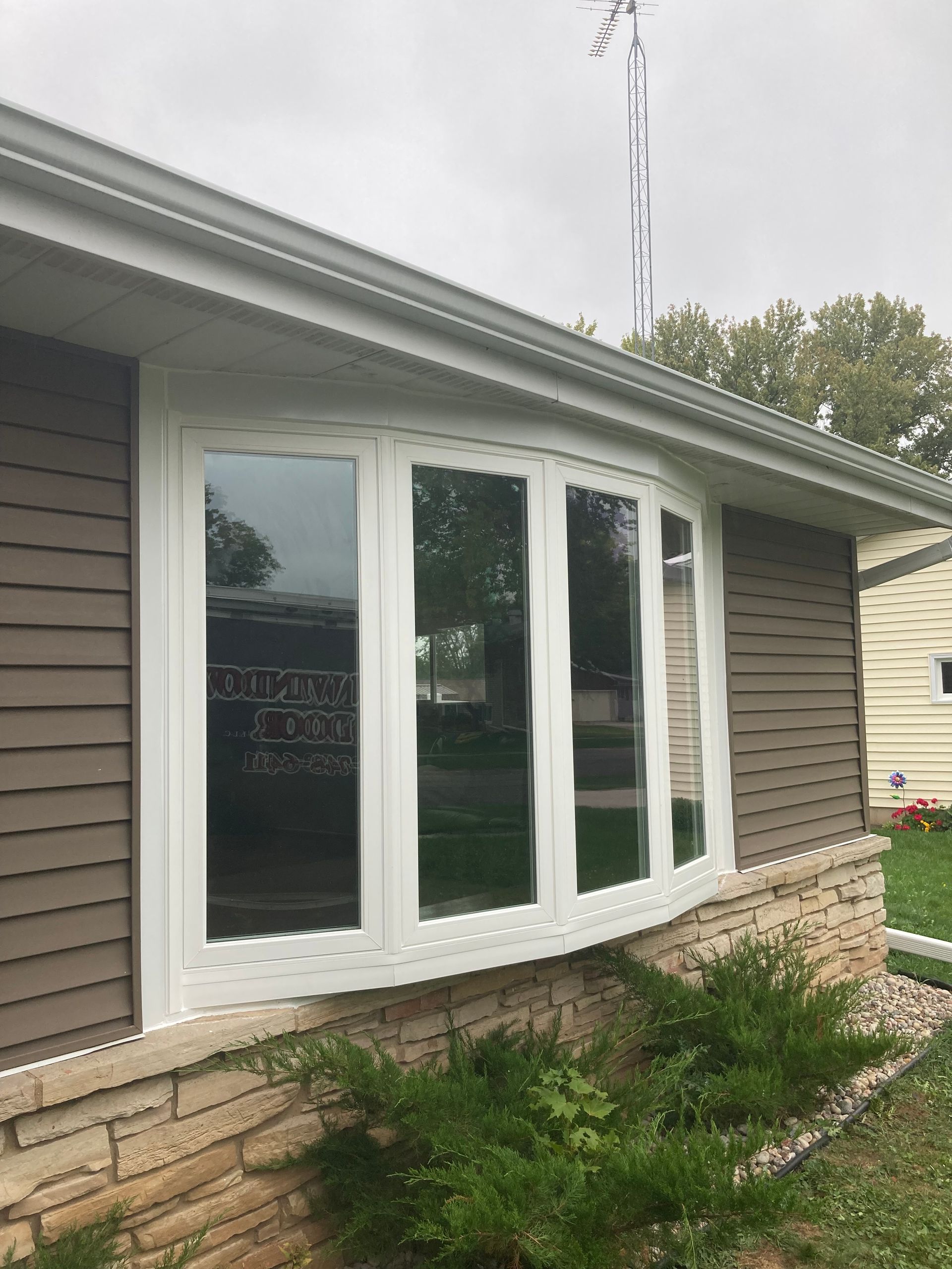 White bay window on a gray house with stone veneer and shrubs in front