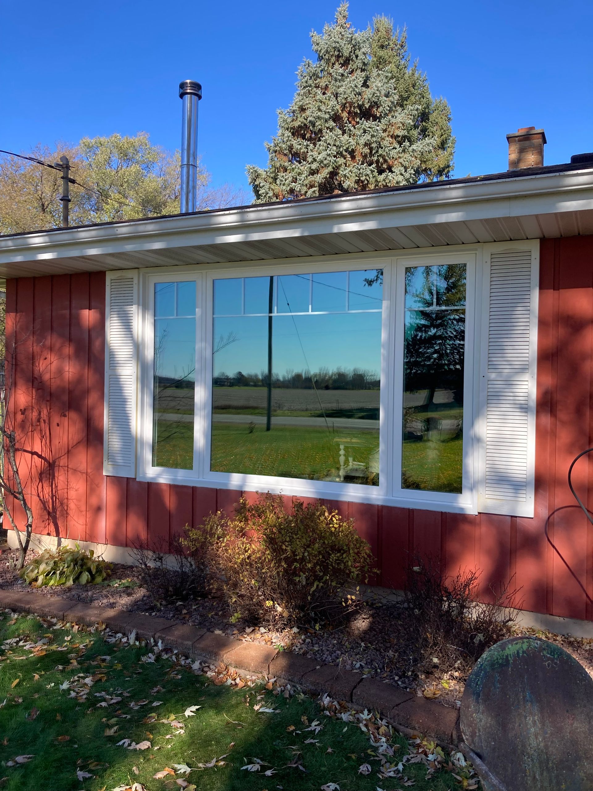 Red house exterior with a white-trimmed window reflecting a grassy field and blue sky.
