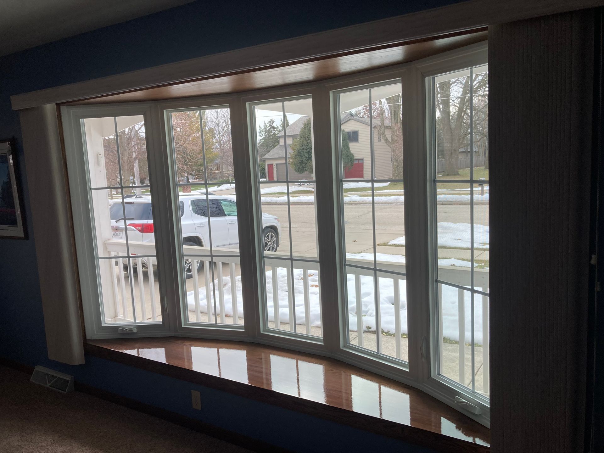Curved bay window with vertical blinds overlooking a snowy residential street
