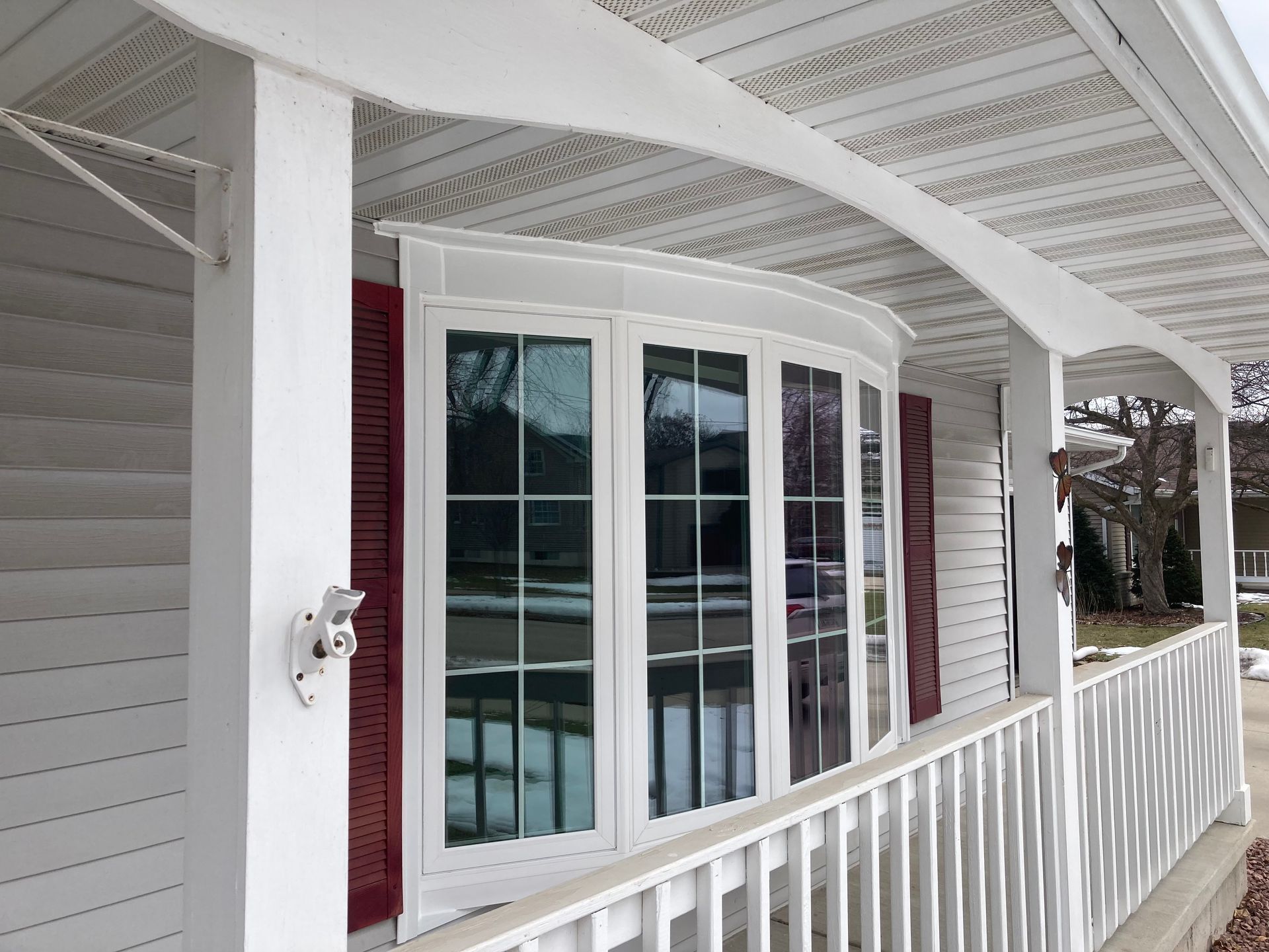 White porch with curved window, red shutters, and white railing on a house exterior
