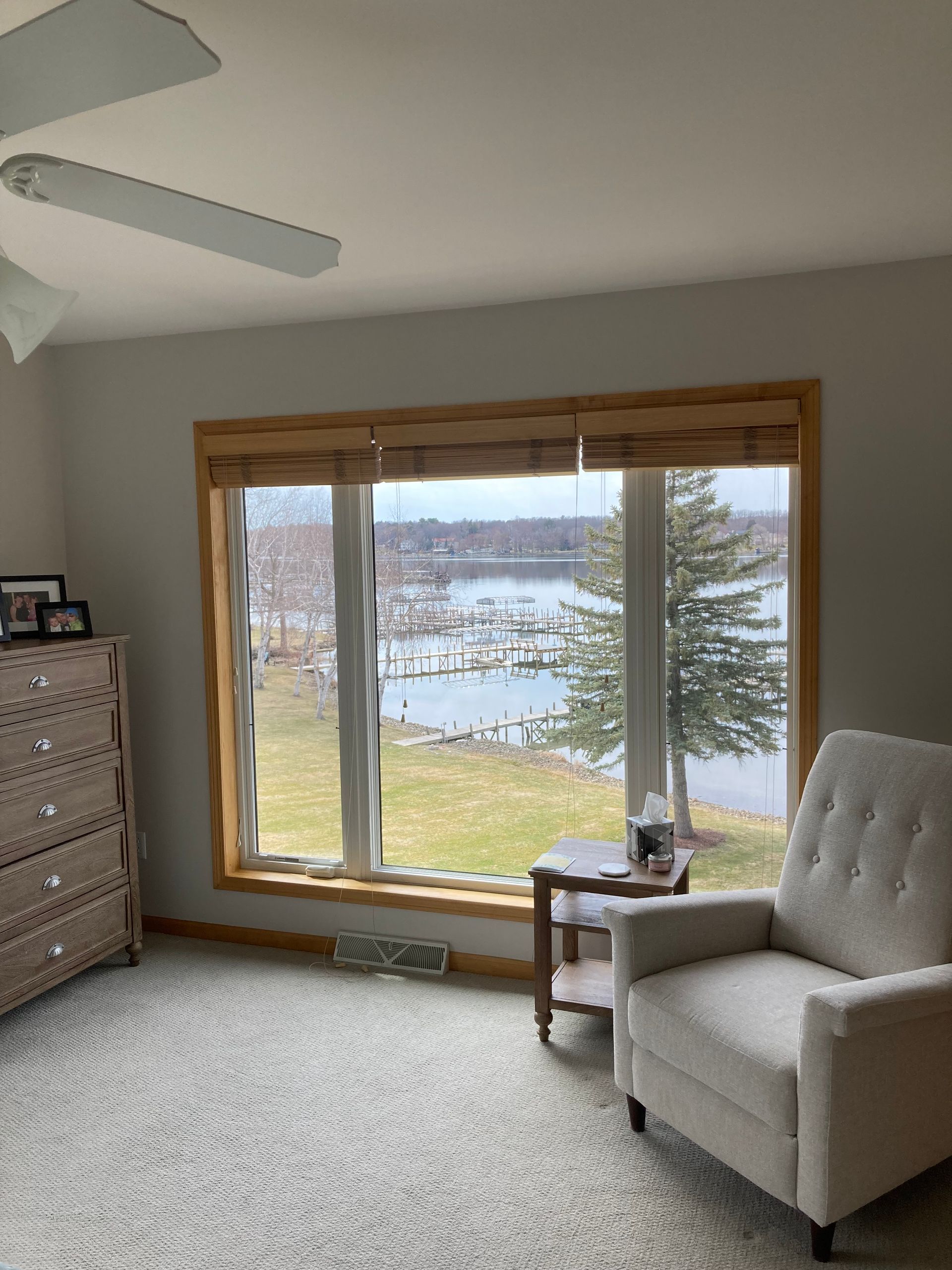 Cozy bedroom with a tufted chair by a large window overlooking water and trees.