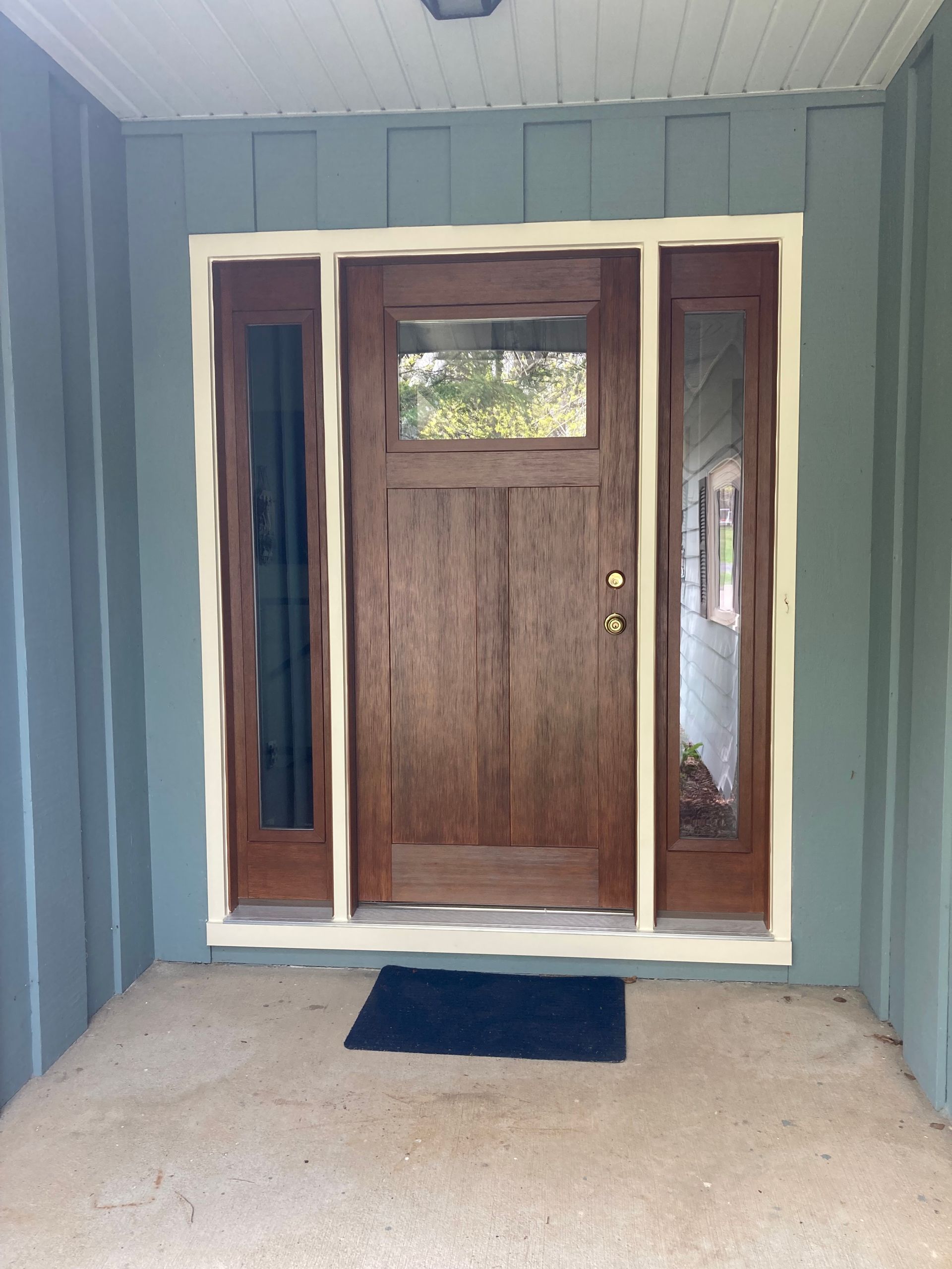 Front porch with a wooden front door, sidelights, blue-gray siding, and a blue doormat.