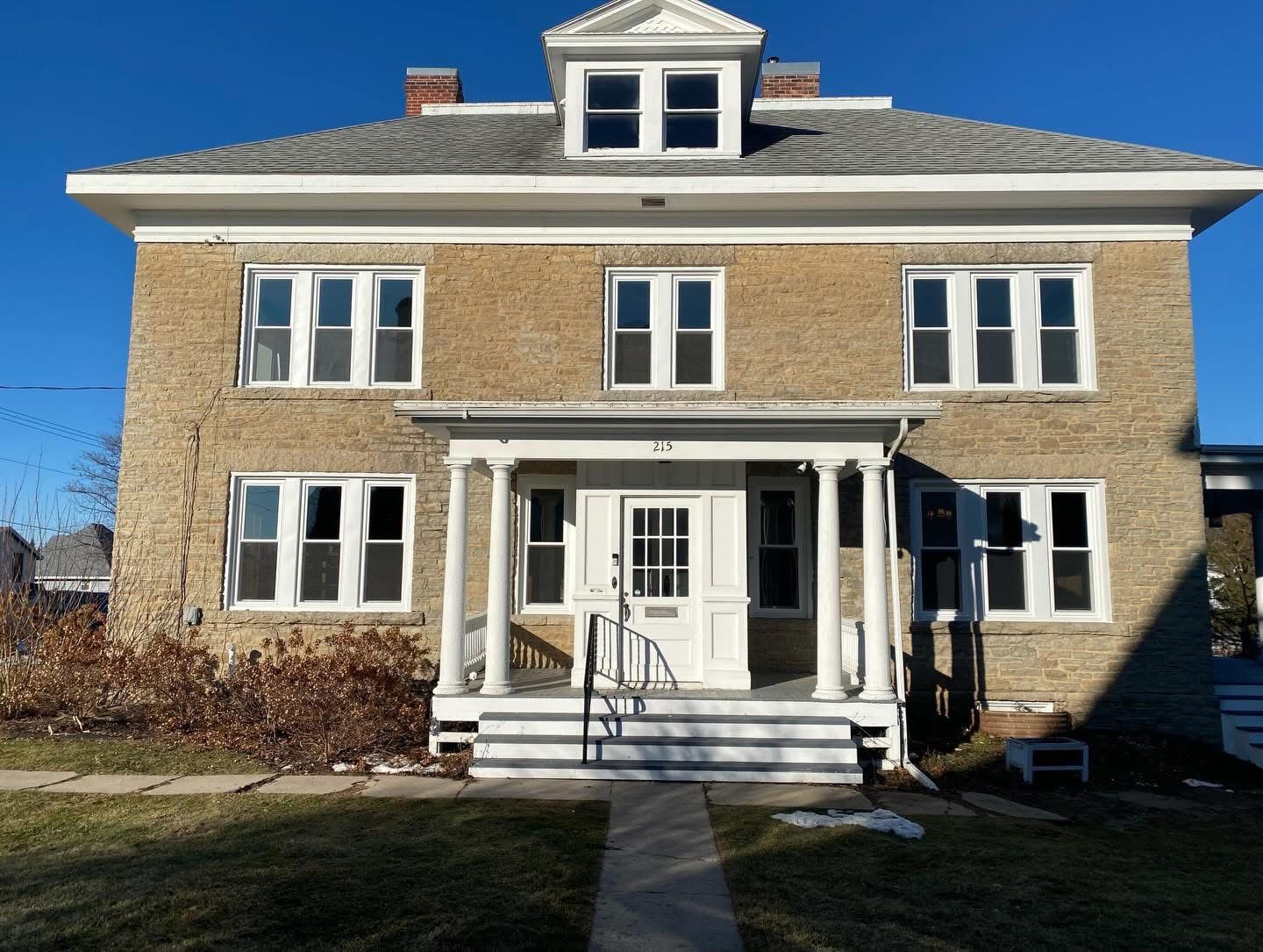 Brick two-story house with white trim, front porch, and dormer windows under a clear blue sky