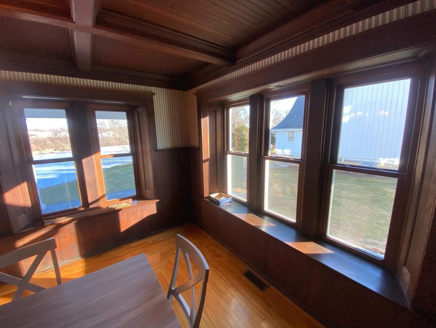 Wood-paneled room with large windows overlooking water and a distant bridge, with a table in the foreground.
