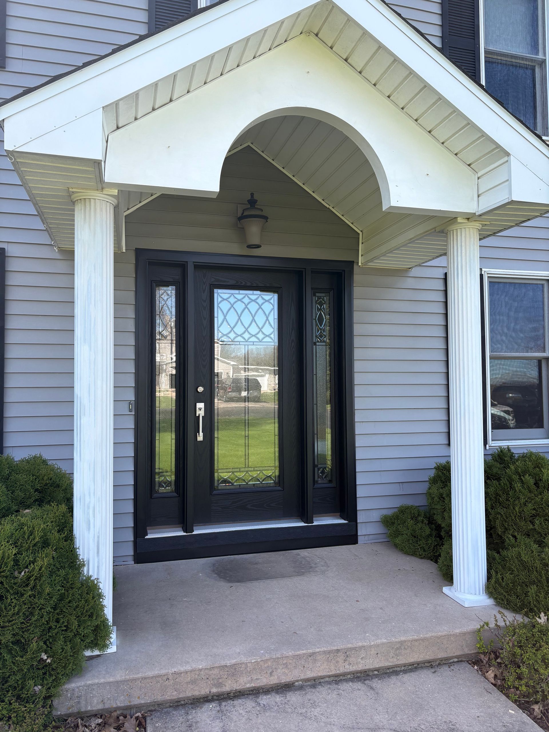 Front entrance with black glass door, white siding, and covered porch with arched awning.