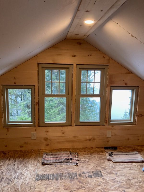 Empty attic room with four windows and unfinished wood walls, lit by a ceiling light.
