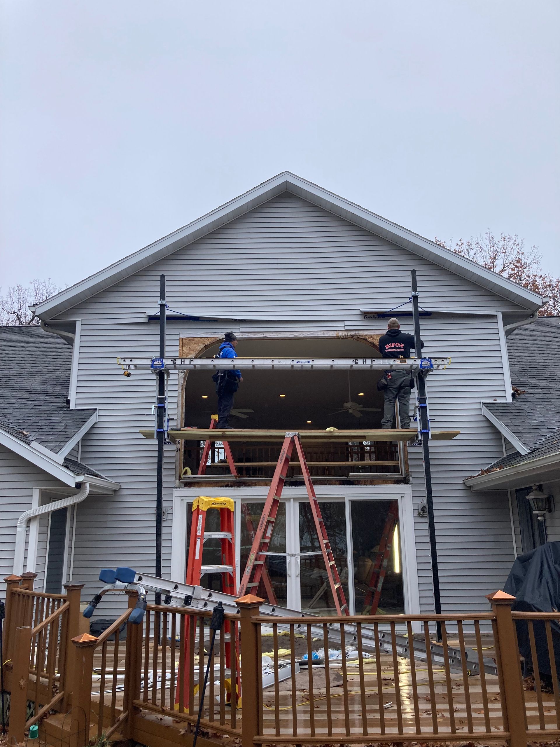 Workers on ladders repairing the front upper porch of a gray house with exposed framing