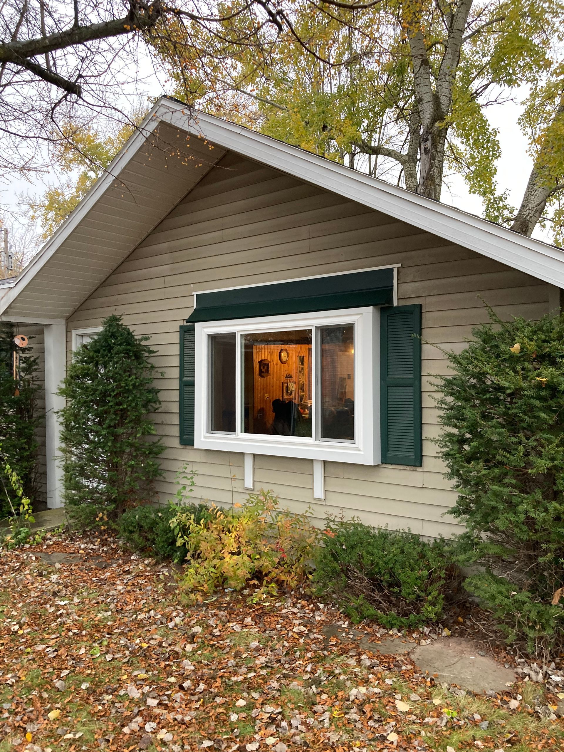 Small beige house with green shutters and an open window amid autumn leaves and trees