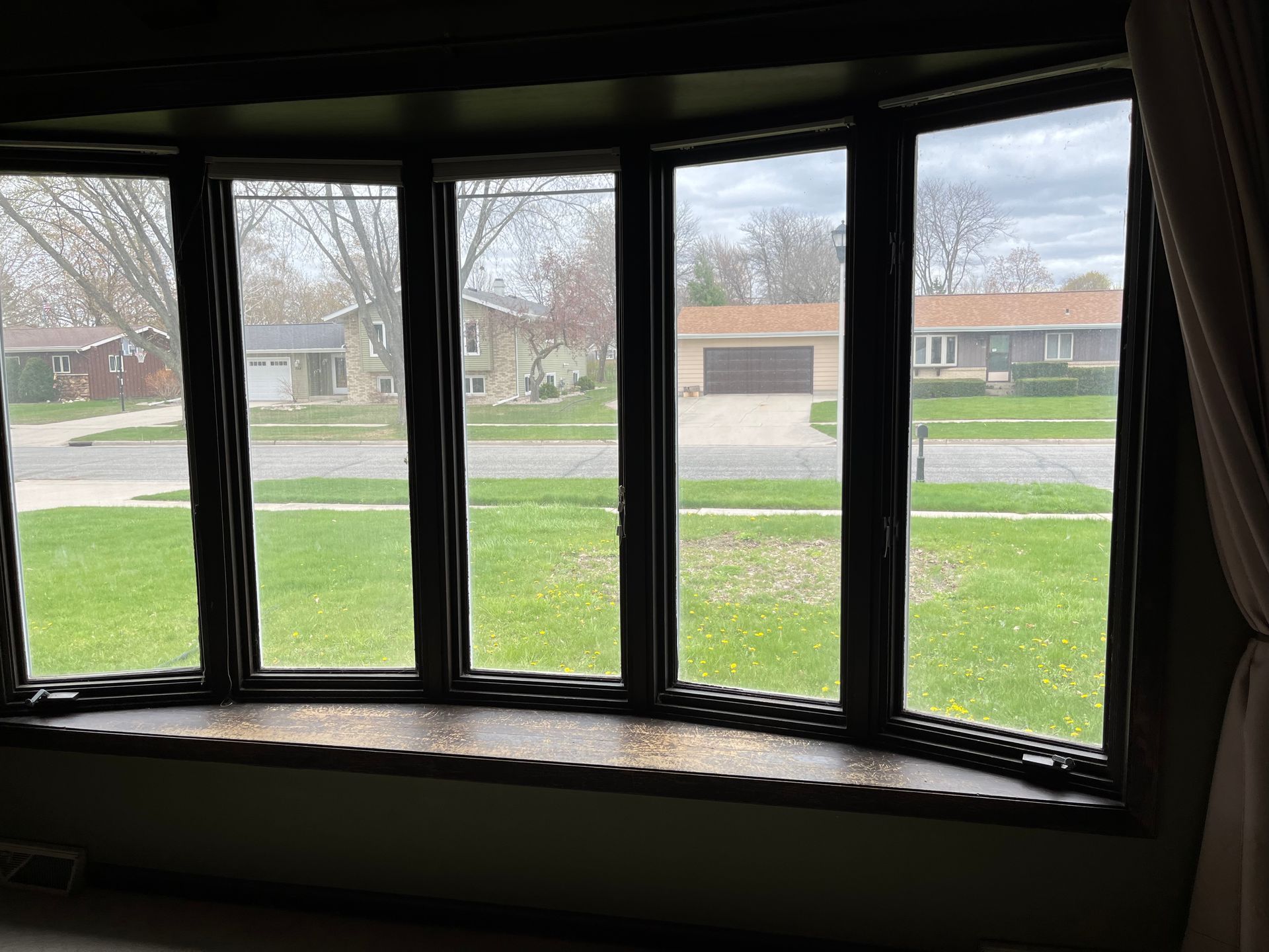 Curved bay window overlooking a green lawn and suburban houses on a quiet street