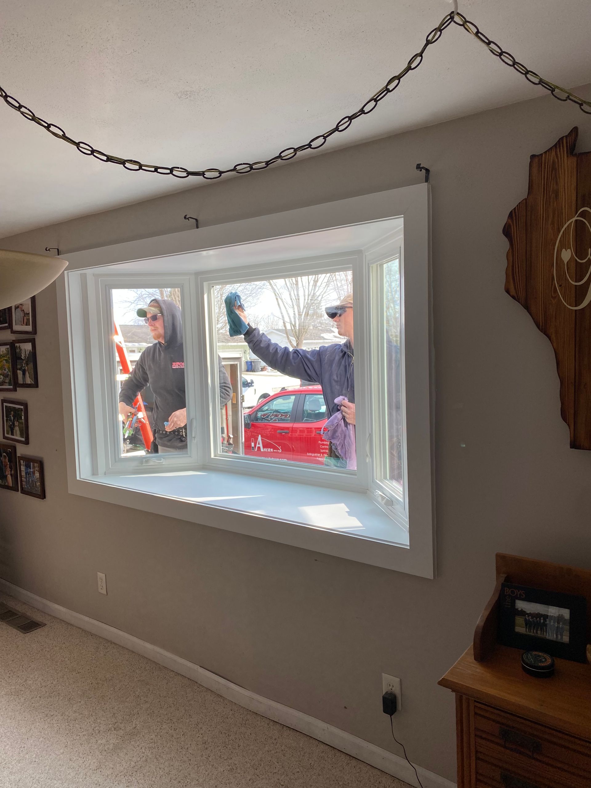 Living room window with people outside, one waving beside a red car
