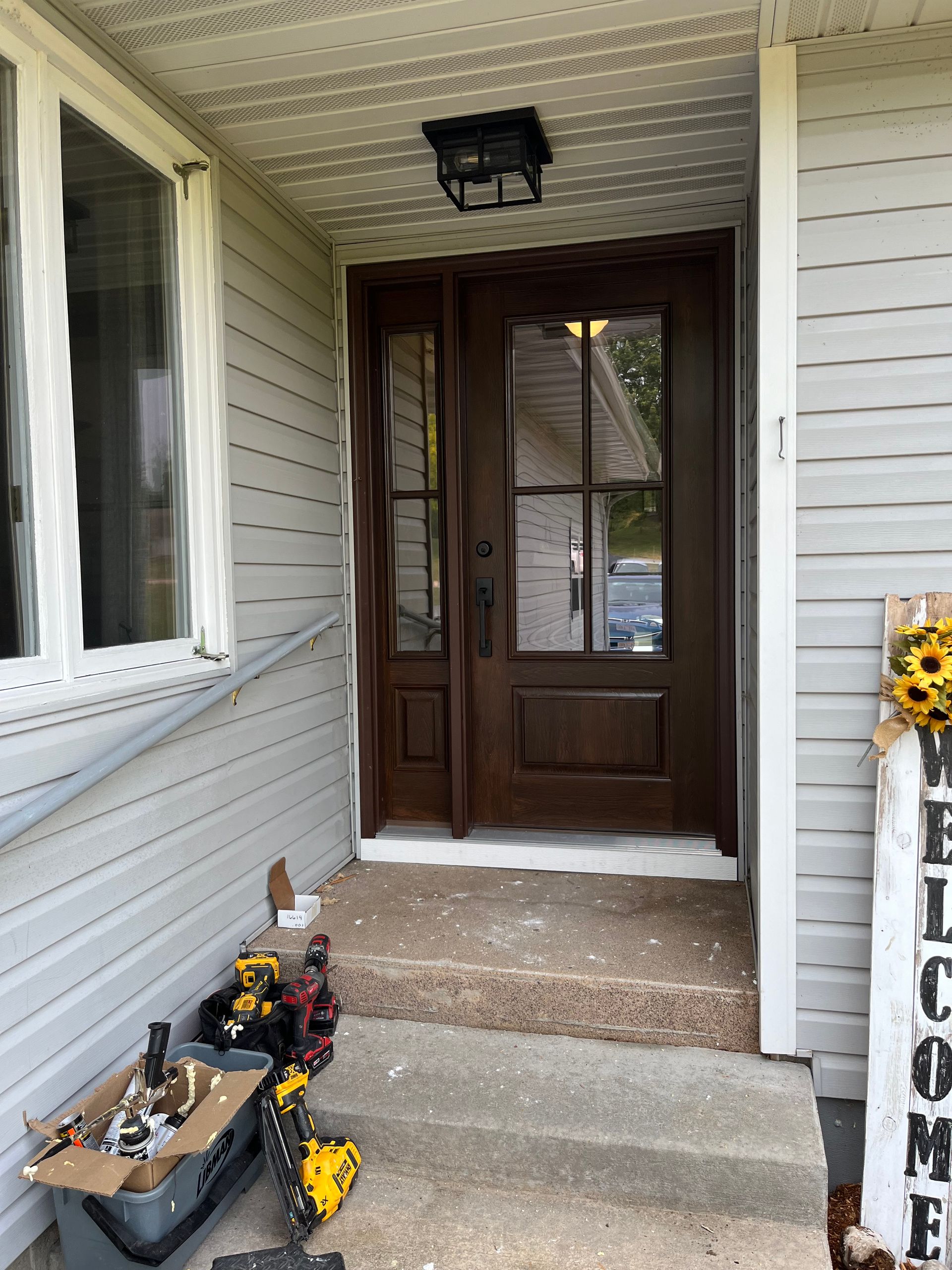 Front porch with dark wooden front door, concrete steps, and potted flowers beside white siding.
