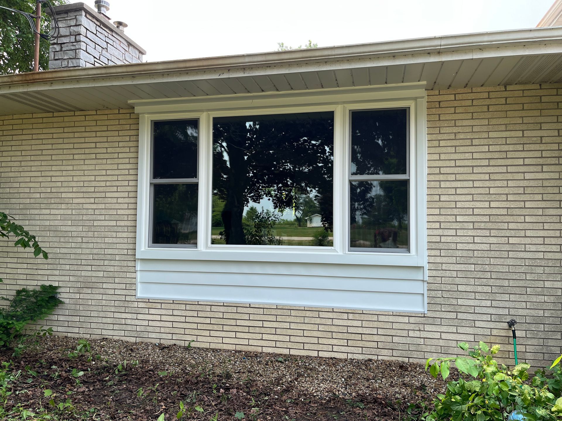 White-trimmed bay window on a beige brick house with a view of trees beyond.
