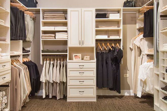Walk-in closet with white cabinets, shelves, hanging clothes, and a central drawer dresser.