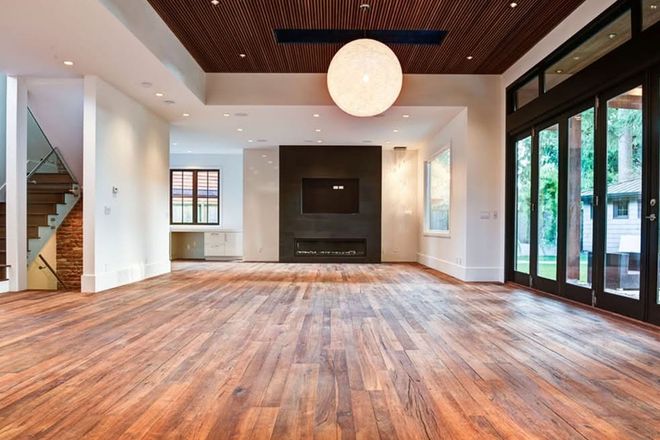 Empty modern living room with wood floors, white walls, dark ceiling, fireplace, and large glass doors
