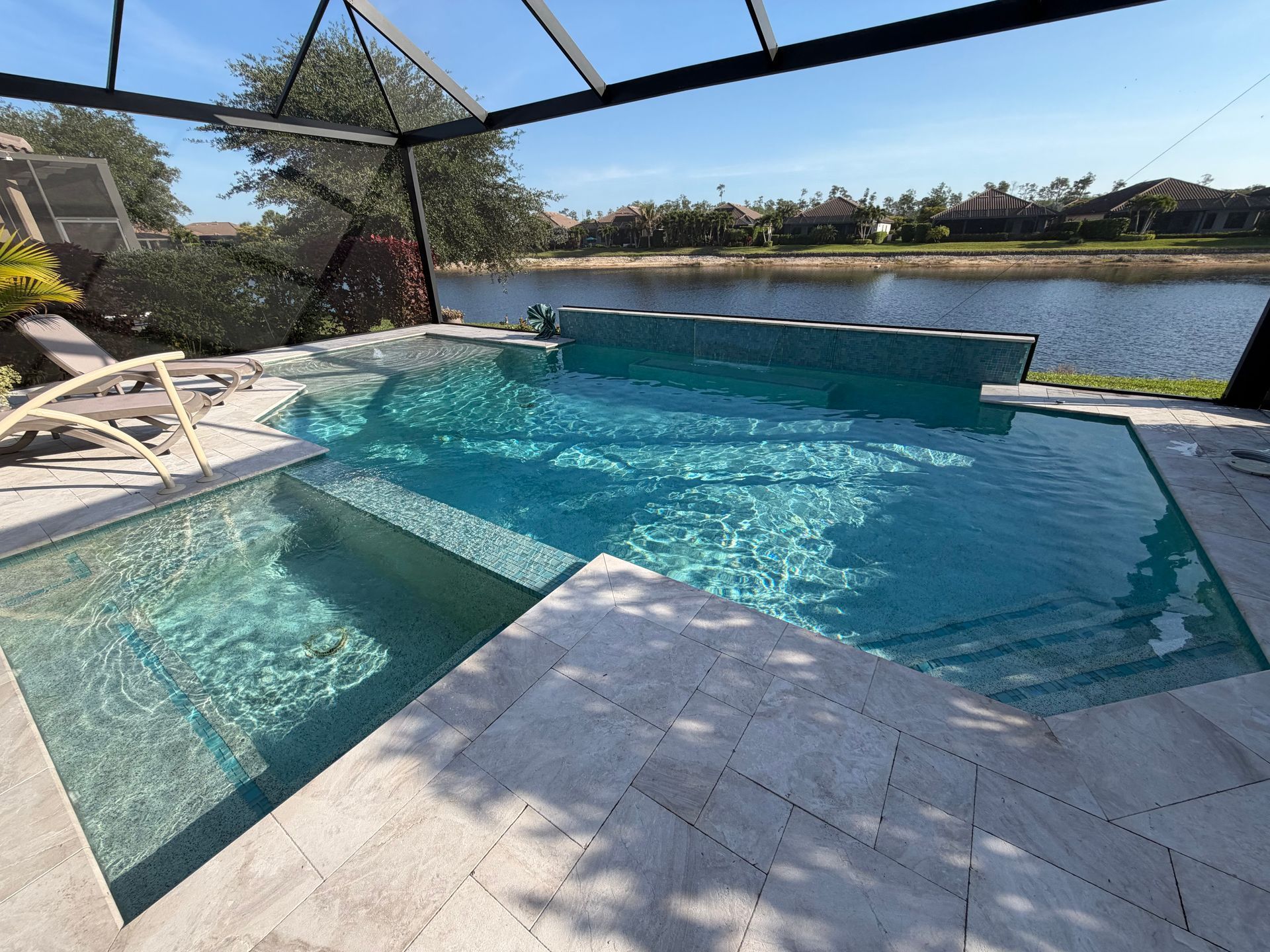 Modern backyard pool with turquoise water, loungers, and a lake view under a screened patio