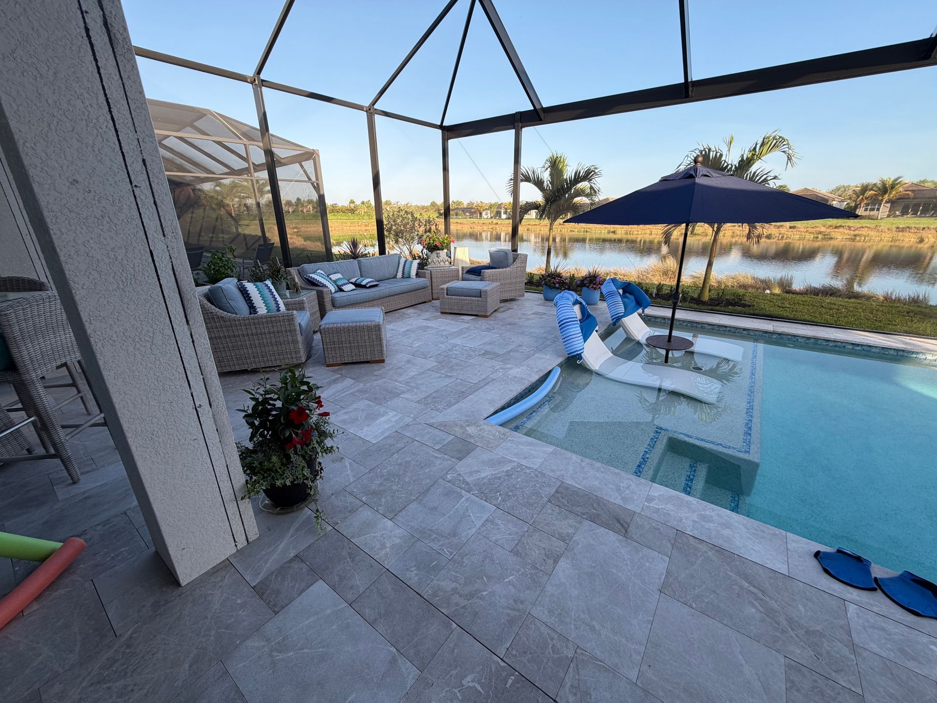 Modern backyard pool patio with lounge chairs, umbrella, and lake view at sunset