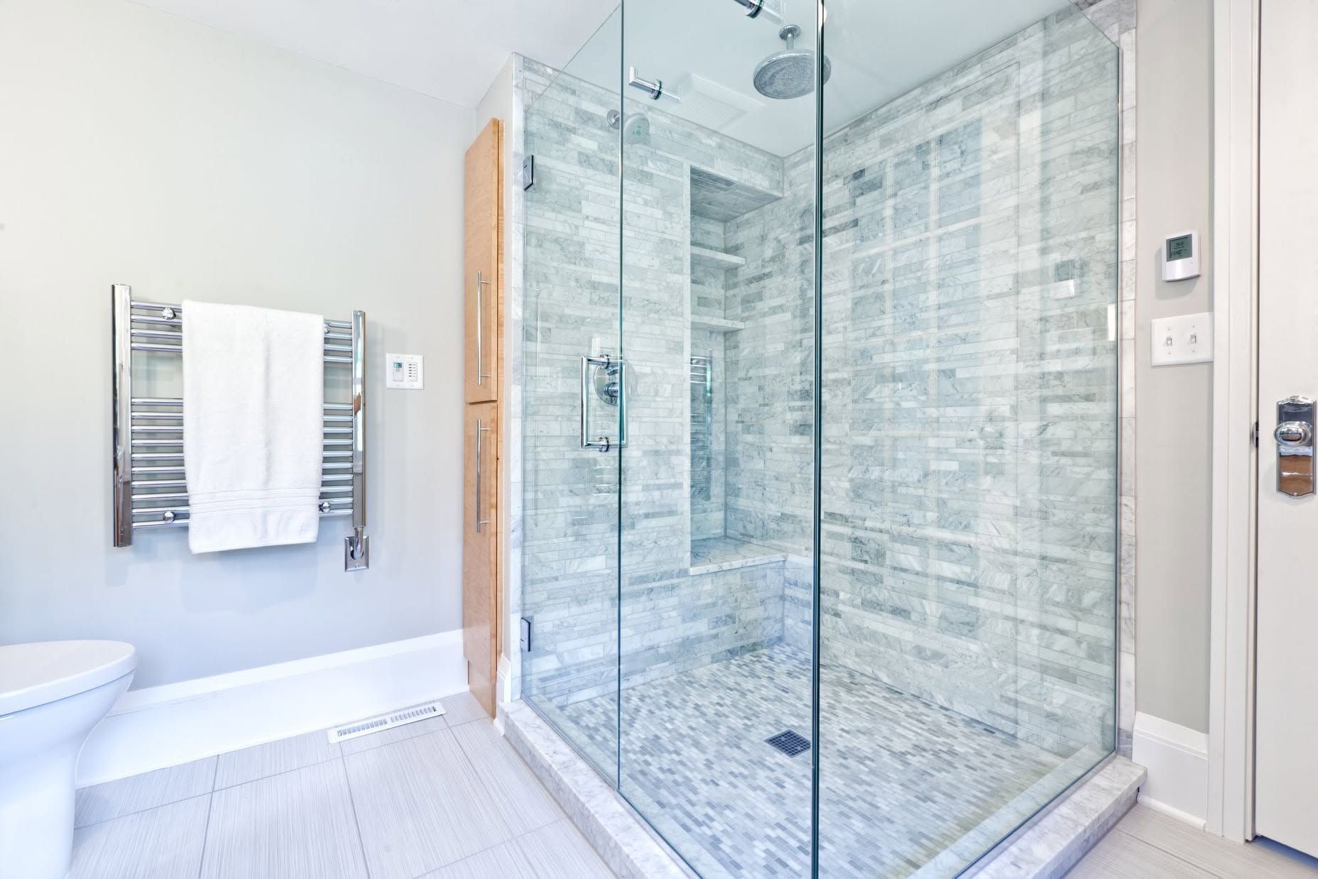 Bright modern bathroom with glass shower, white tile, and towel rack by the bathtub