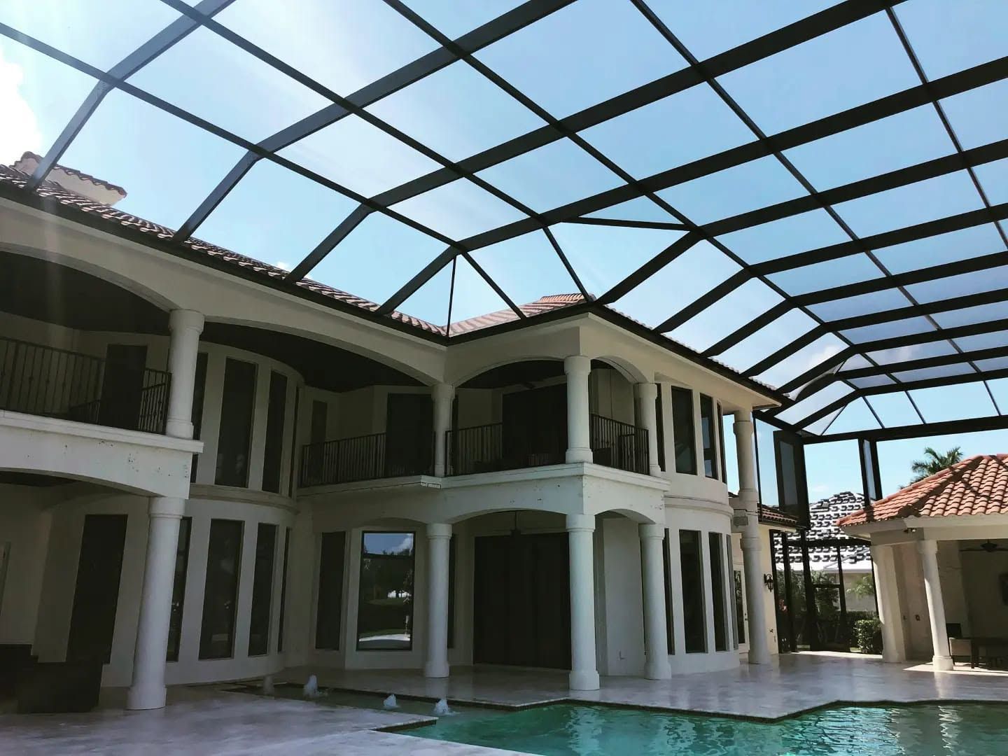 Modern two-story house with a large screened patio and tiled pool area under a glass roof