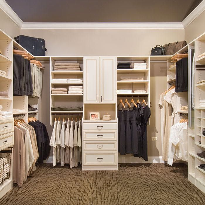 Spacious walk-in closet with white shelving, hanging clothes, drawers, and folded linens on beige carpet.