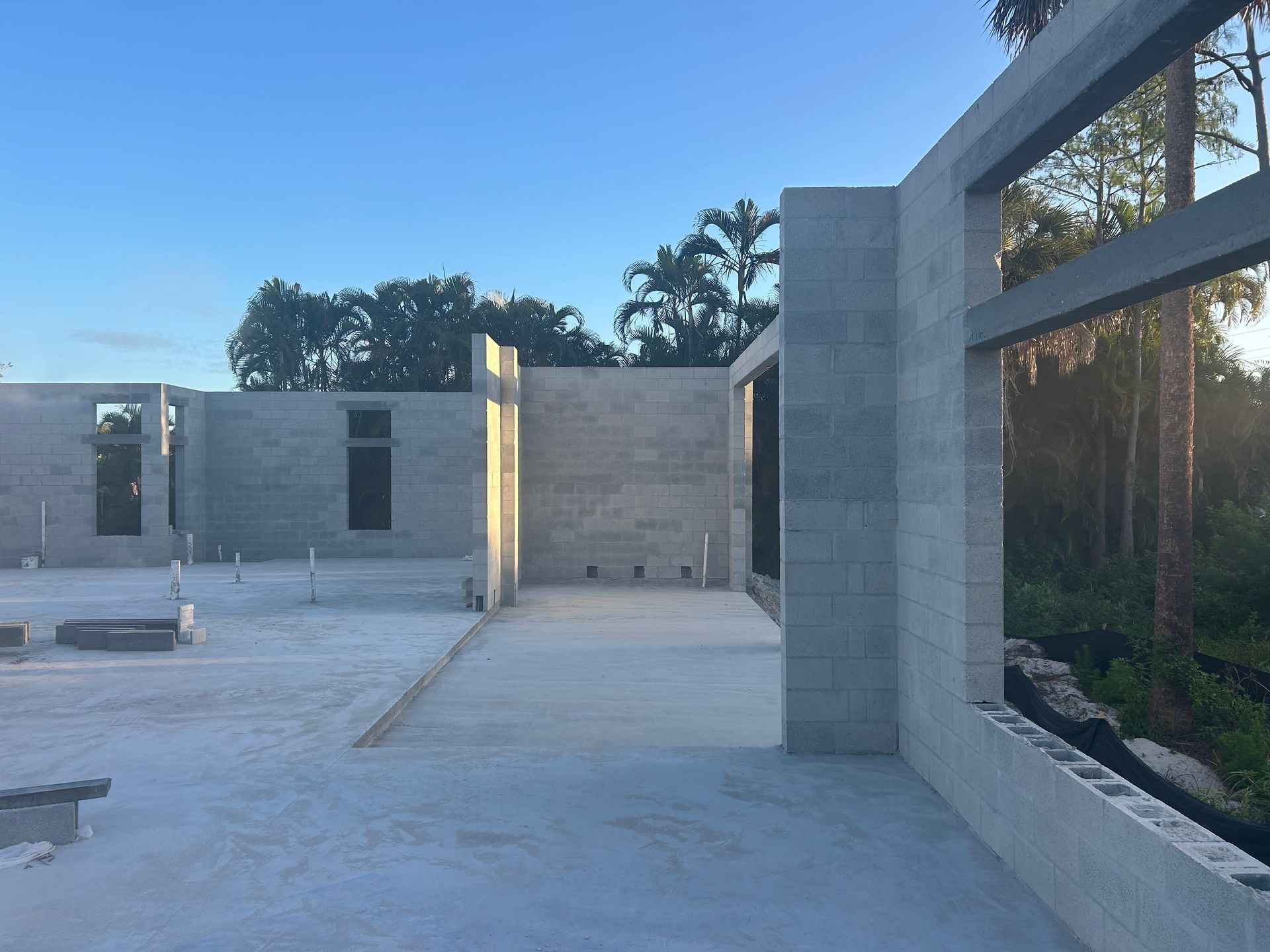 Construction site with concrete block walls and open roof framing at sunset.