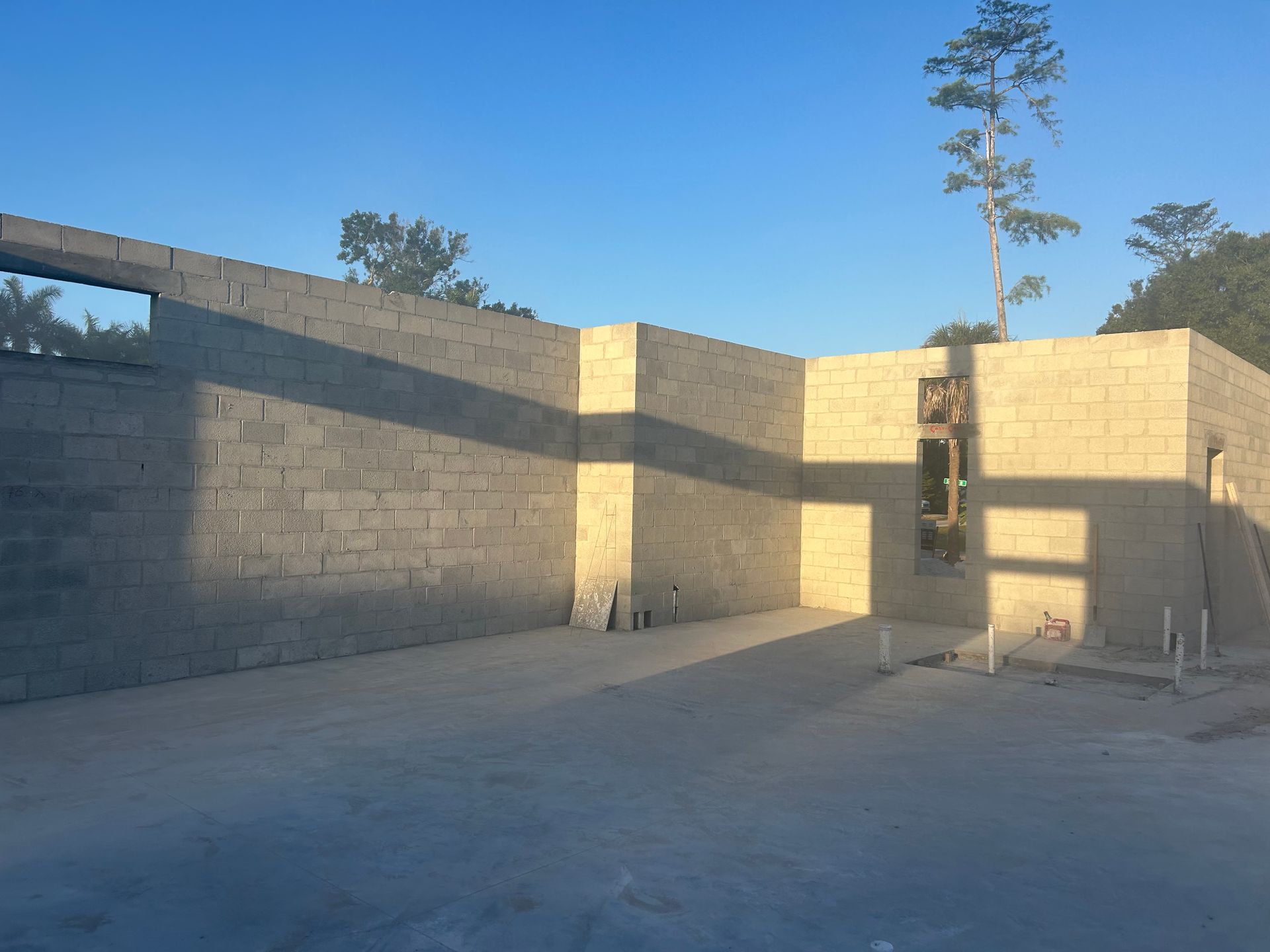 Unfinished tan brick building walls around an empty concrete floor under a clear blue sky