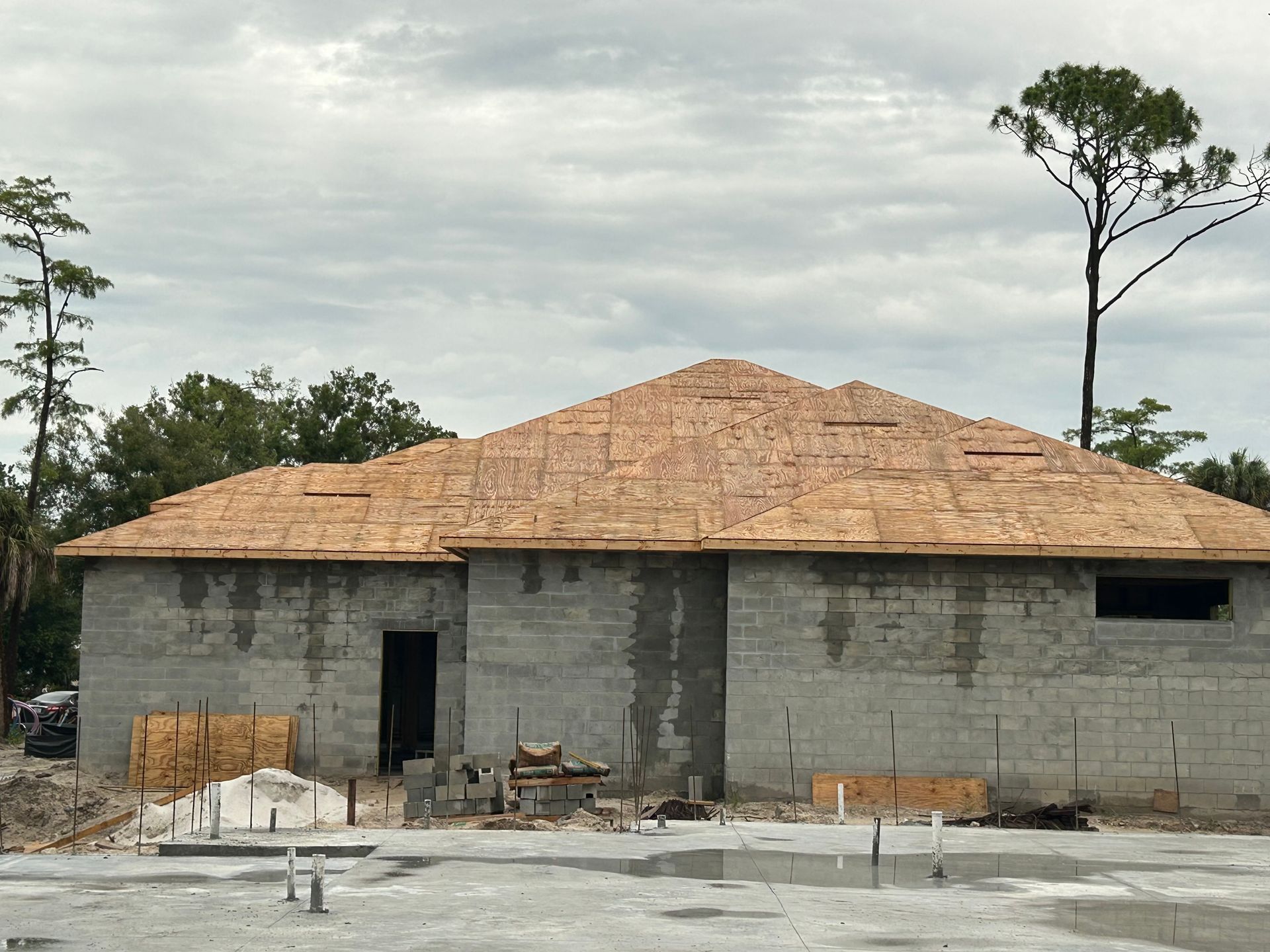 Unfinished concrete house with a tan roof under construction amid trees and cloudy sky