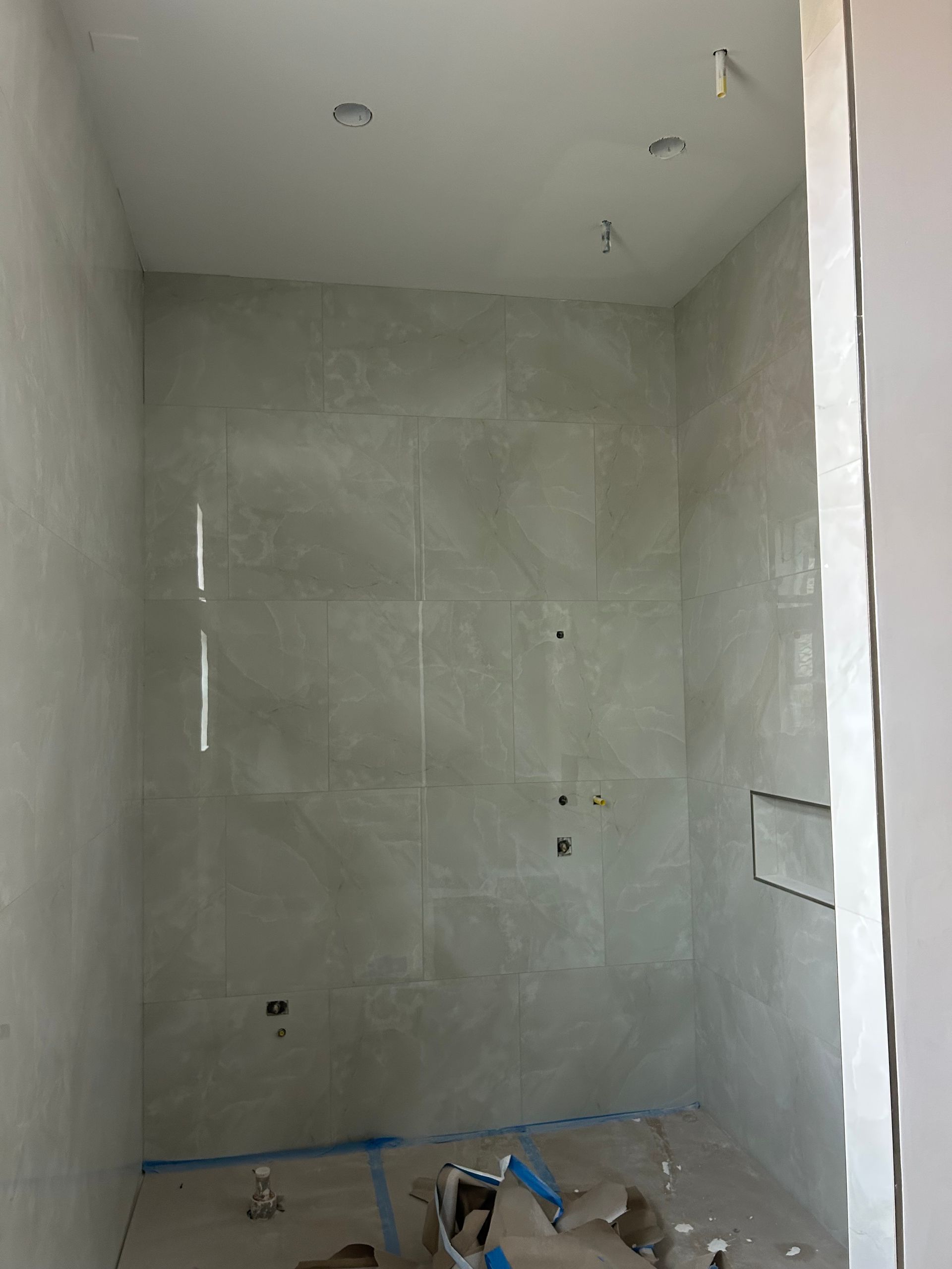 Small tiled bathroom under construction with unfinished walls, exposed fixtures, and tools on the floor