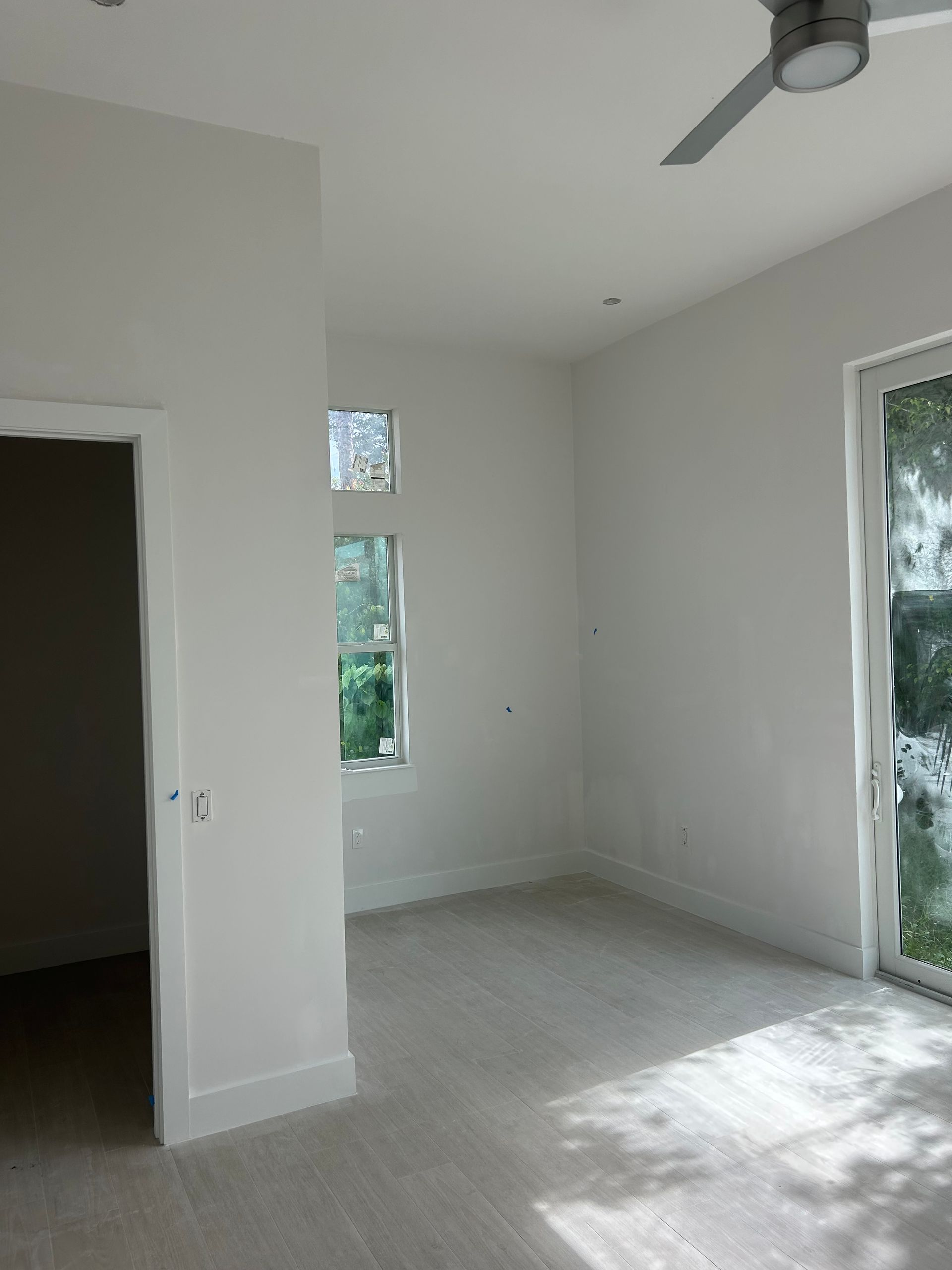 Empty white room with a ceiling fan, small windows, and a sliding glass door letting in sunlight.