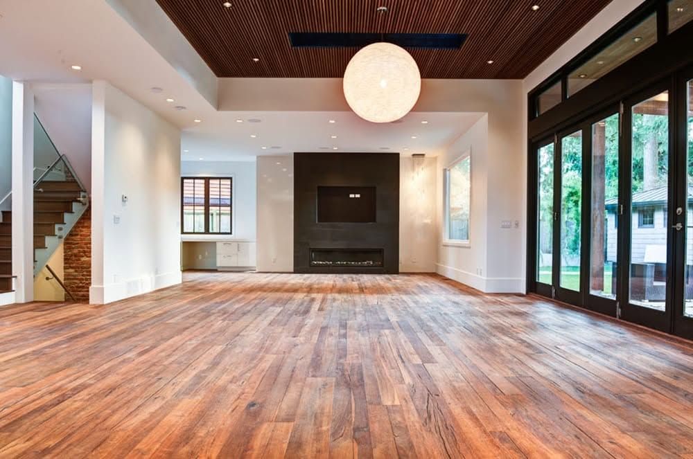 Empty modern living room with wood floors, white walls, dark ceiling, and large windows.