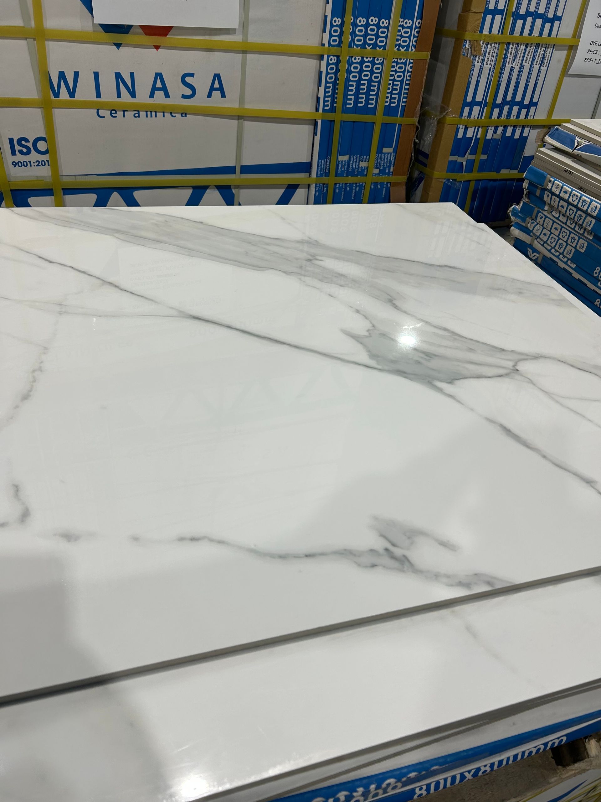 White marble-look tile slabs stacked on a blue metal rack in a warehouse