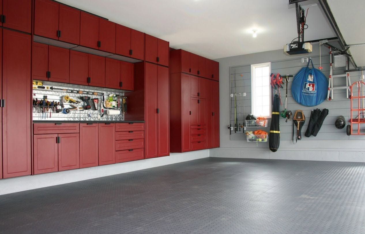 Spacious garage with red storage cabinets, wall tools, a bike, and a gray floor.