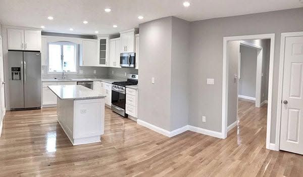 Bright, modern open kitchen with white cabinets, island, stainless appliances, and light wood floors.