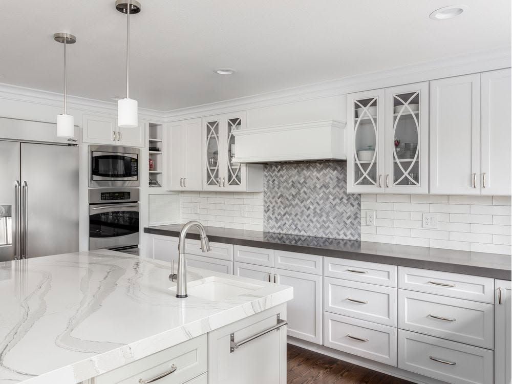 Bright white modern kitchen with island, marble countertop, gray backsplash, and stainless steel appliances