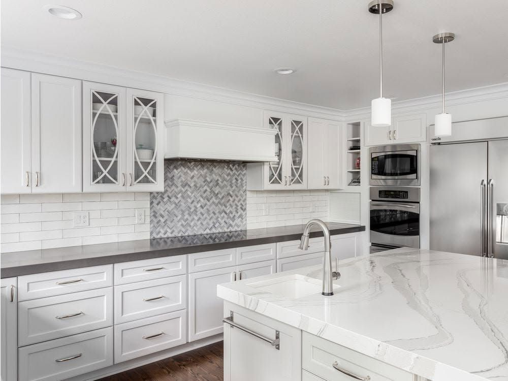 Bright white modern kitchen with marble island, stainless appliances, and gray mosaic backsplash