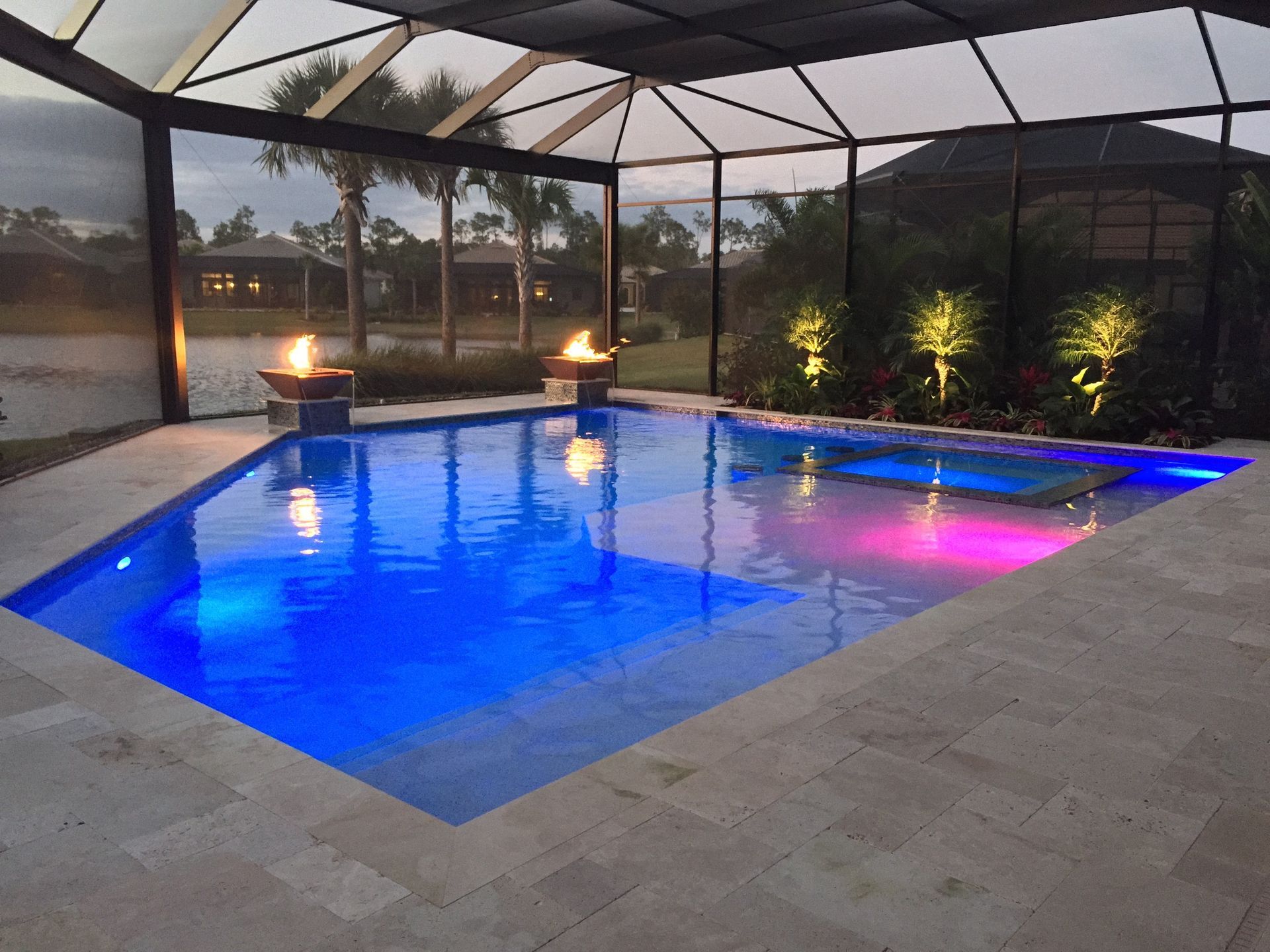 Illuminated backyard pool at dusk with blue water and warm accent lights near screened patio.