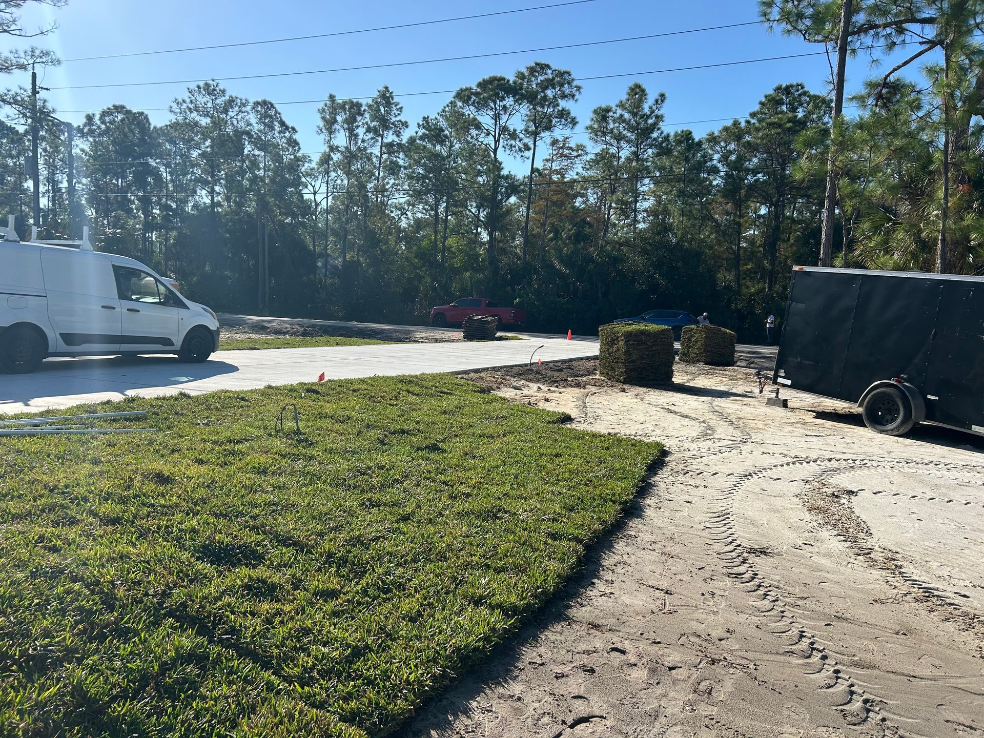 Sunny roadside lot with a white truck, sand path, green grass, and trees in the background