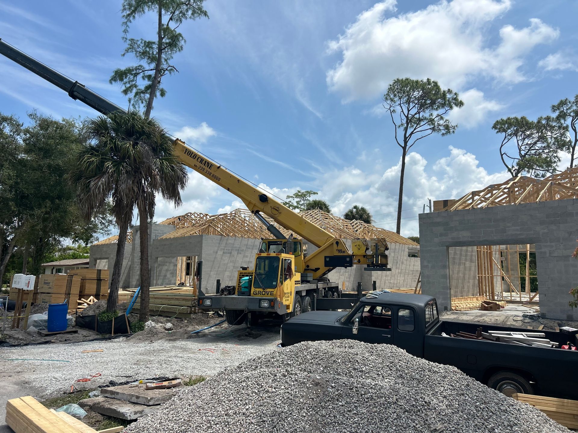 Construction site with a yellow crane lifting materials beside unfinished stone buildings and a black pickup truck