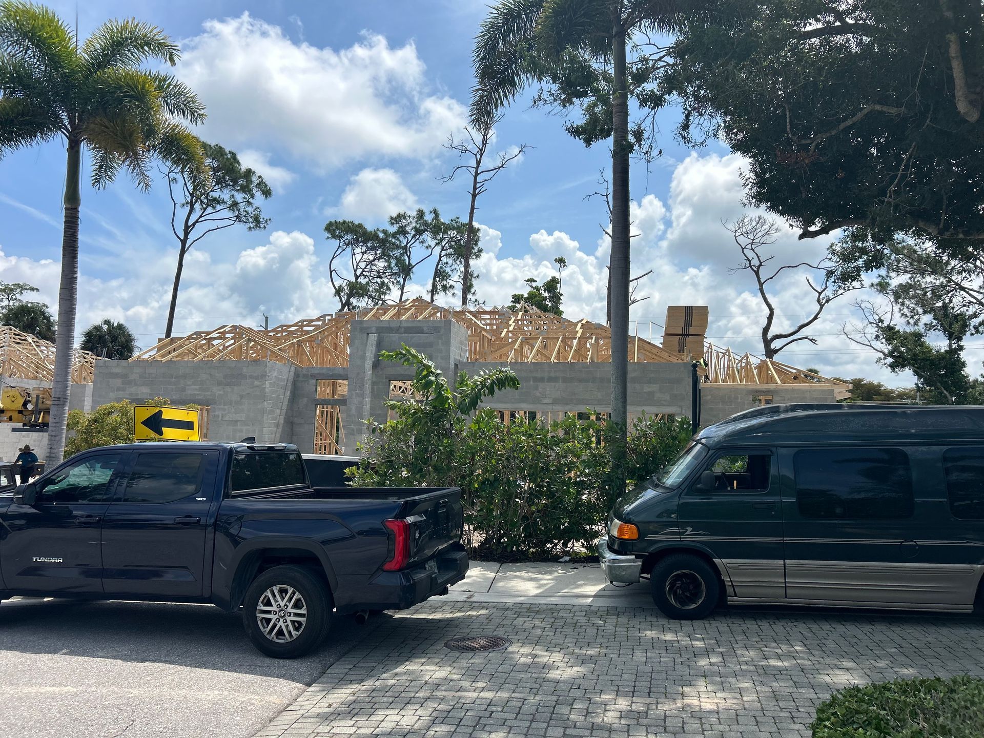 Two parked trucks by a stone wall and trees under a bright blue sky