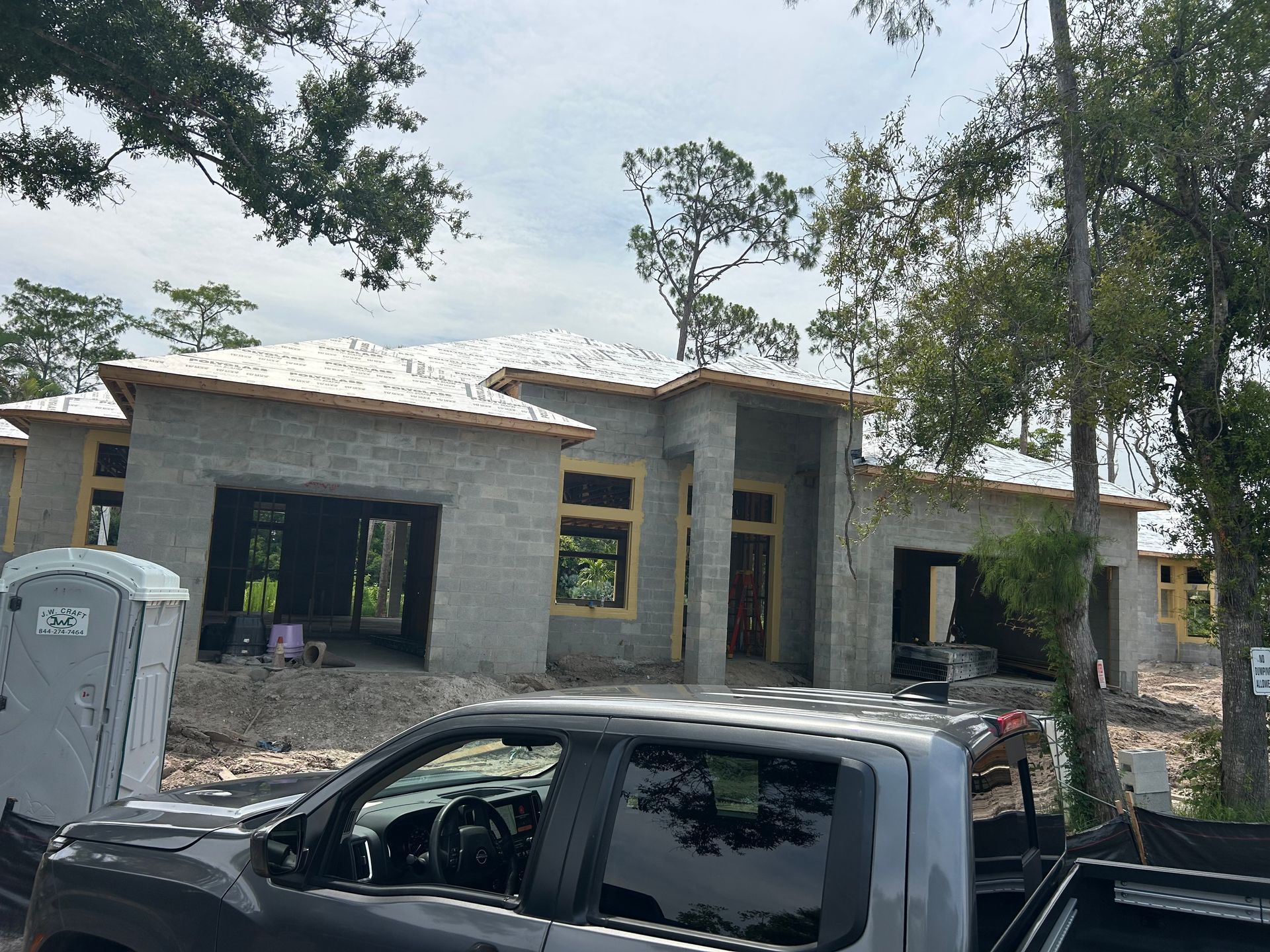 Partially built gray stone house with a black pickup truck parked in front and trees overhead