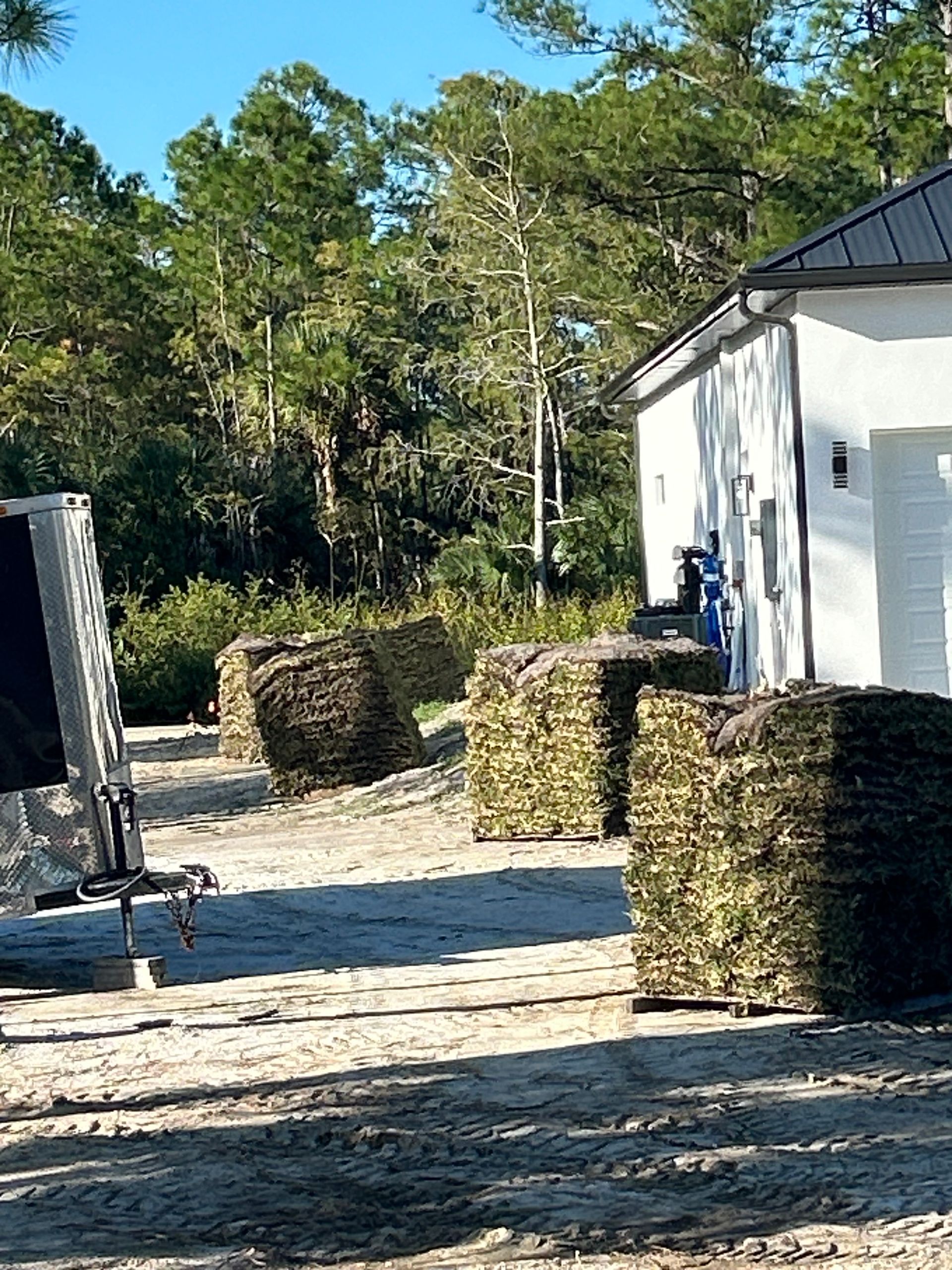 Outdoor shooting range with hay bale barriers, a dirt path, and a white building beside trees