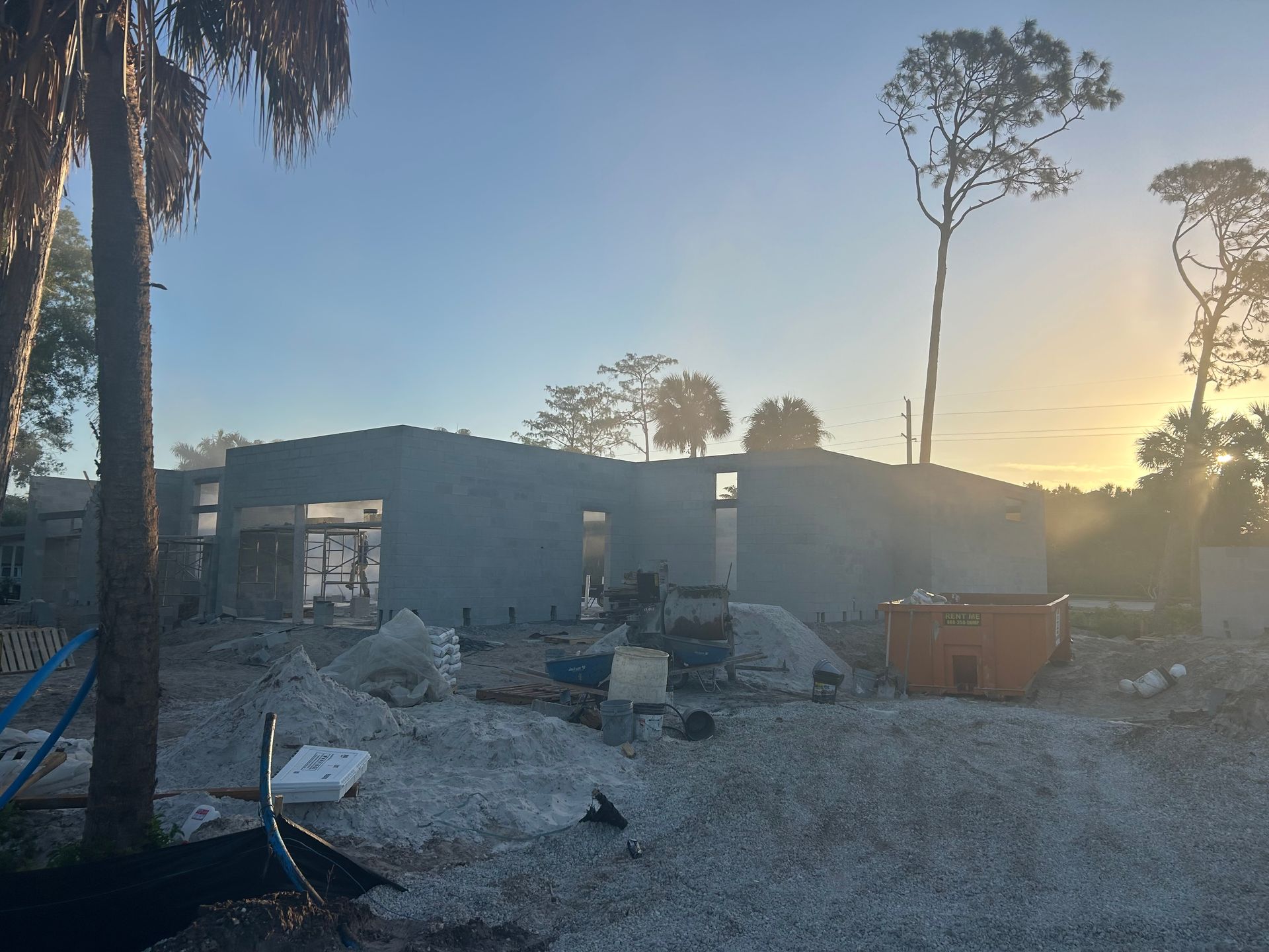 Partially destroyed building amid rubble at sunset, with palm trees and a large dumpster nearby