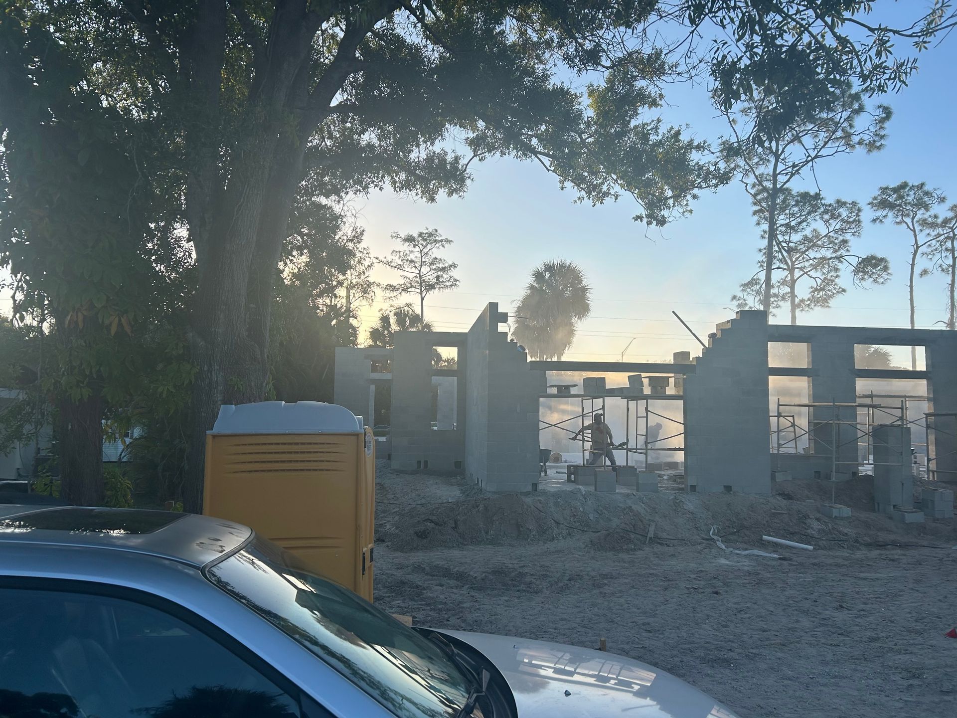 Partially burned building with rubble, smoke, and a parked car in the foreground at dusk