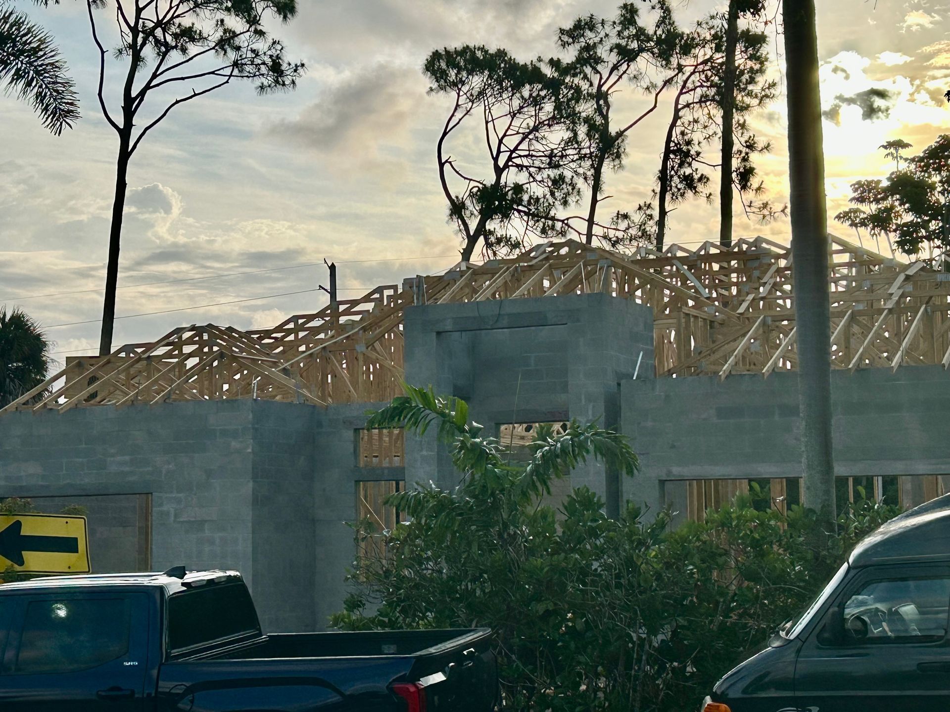 Partially built house with exposed wooden roof framing behind a concrete wall at sunset