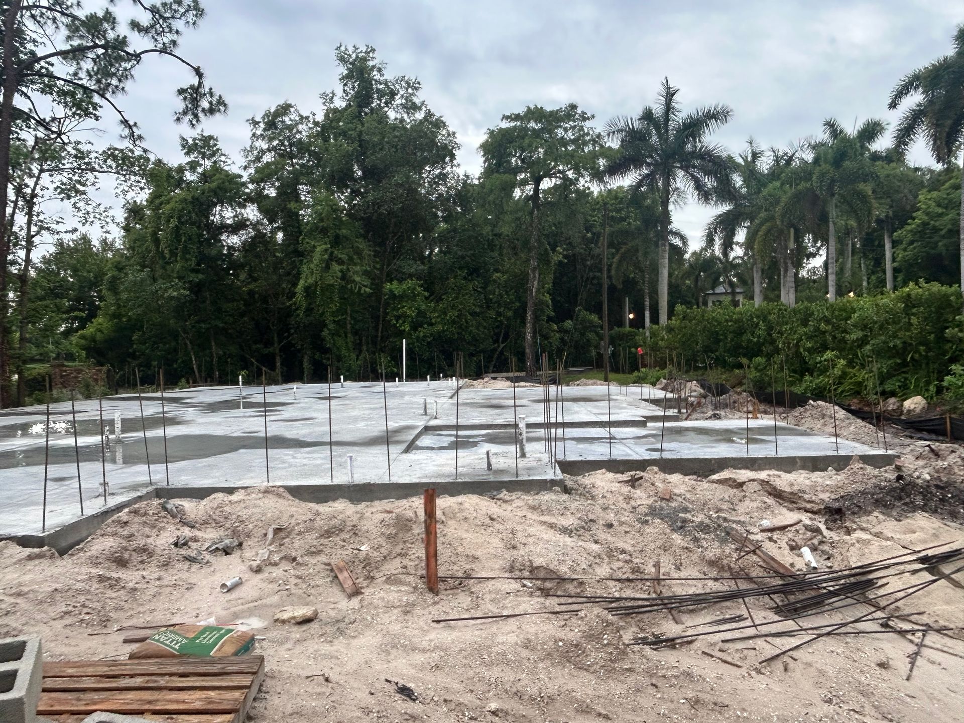 Concrete foundation slab under construction in a cleared site with trees in the background
