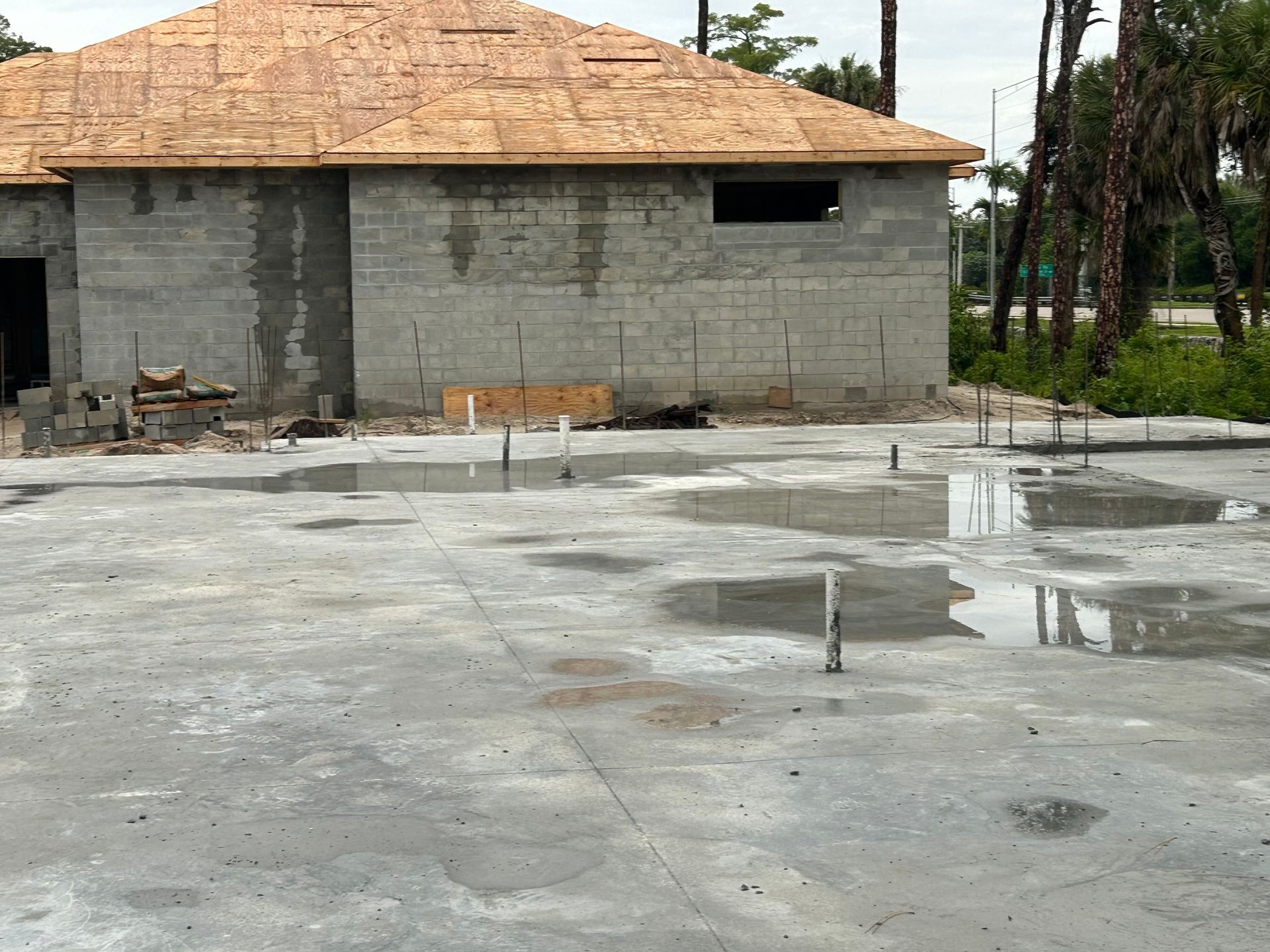 Unfinished concrete courtyard beside a gray cinderblock house with a tan tiled roof and wet patches.