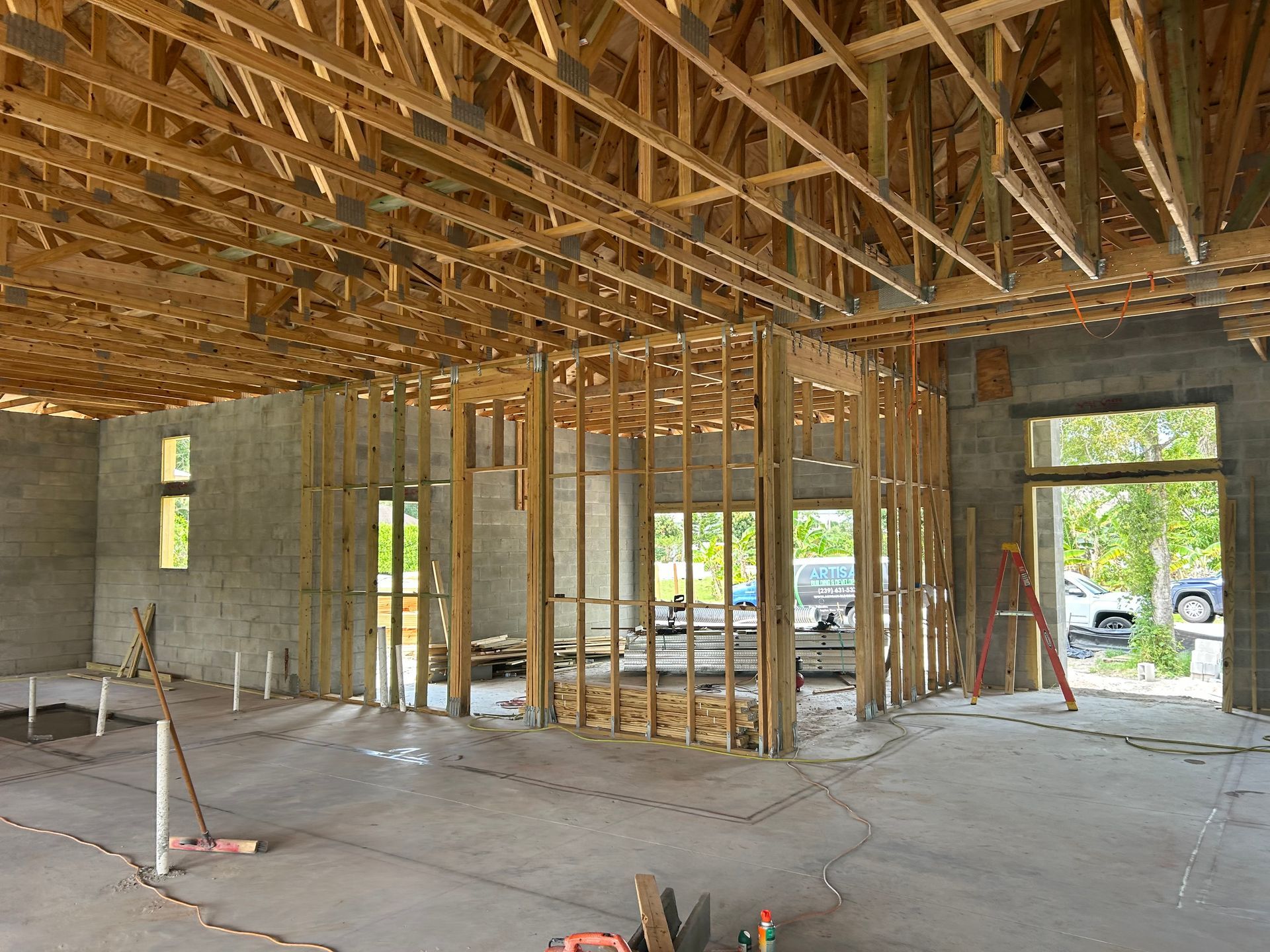 Unfinished house interior with exposed wooden roof trusses, concrete walls, and open window and door frames