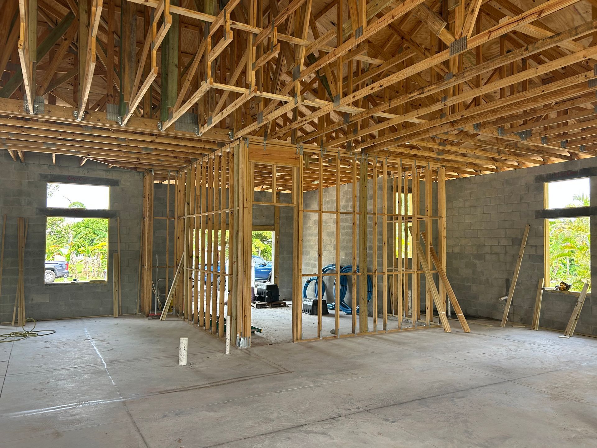 Unfinished house interior with exposed wooden framing, concrete walls, and open window and door openings.