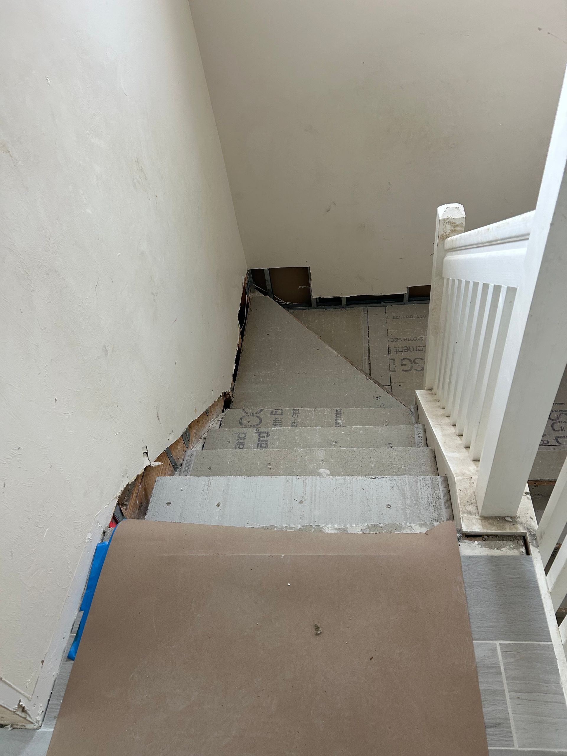 Narrow stairwell with concrete steps, white railing, and beige walls leading down.