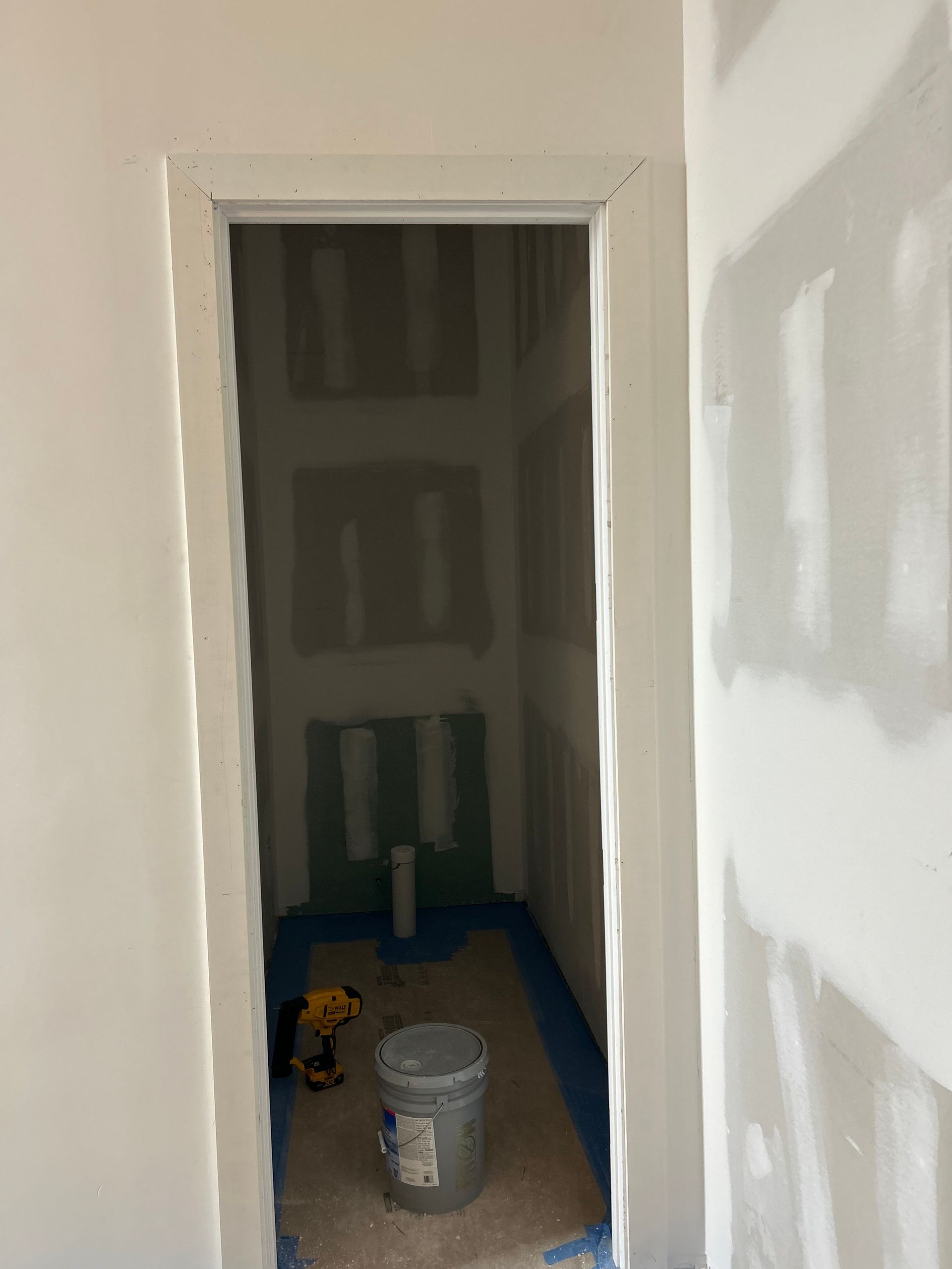Partially finished doorway into a drywall room with construction buckets and tools on the floor